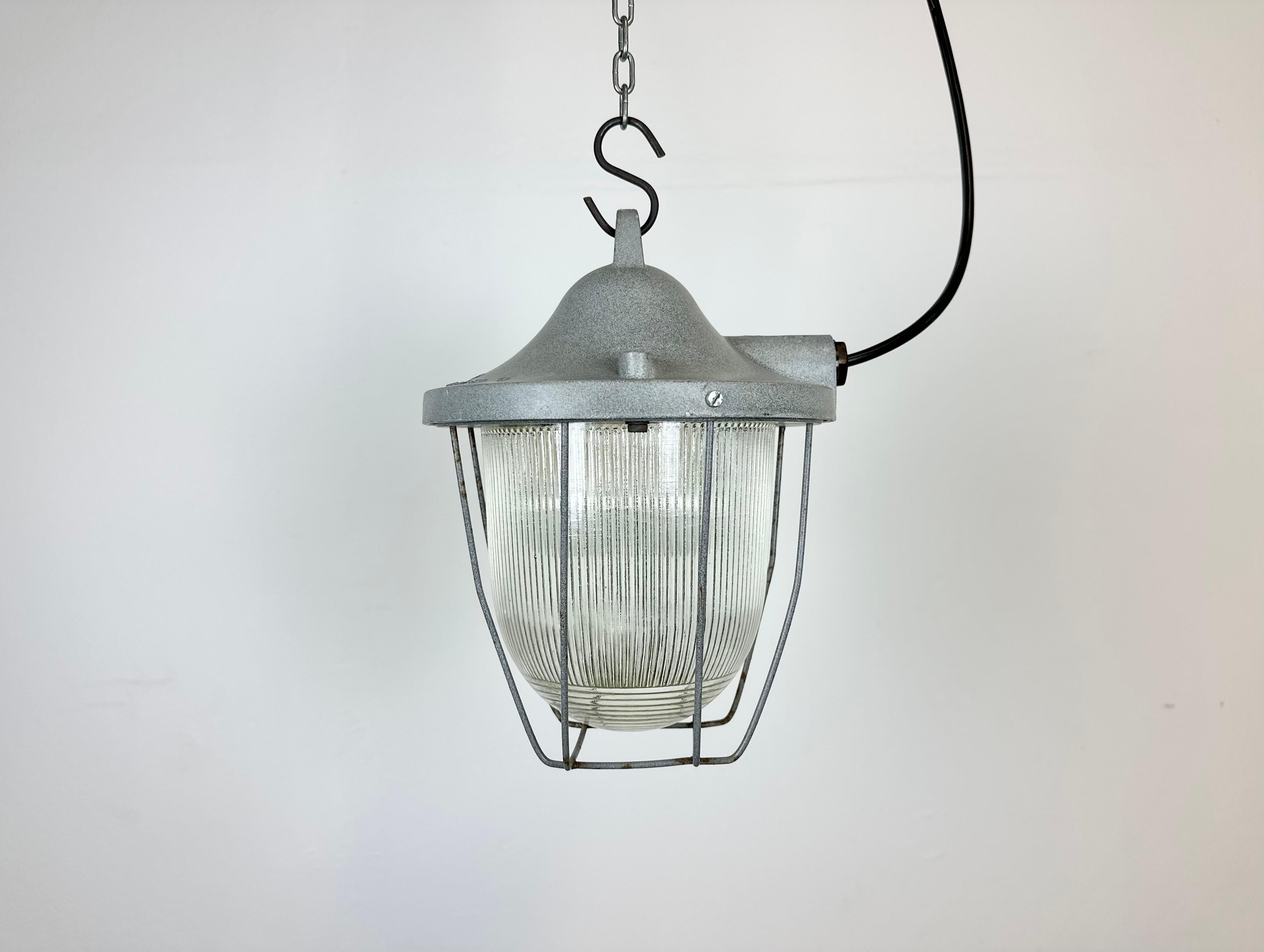 Grey industrial lamp made by Polam Gdansk in Poland during the 1960s. It features a cast aluminium body, an iron cage and striped glass. The porcelain socket requires E 27/ E 26 lightbulbs. New wire. The weight of the lamp is 2,5 kg.
   