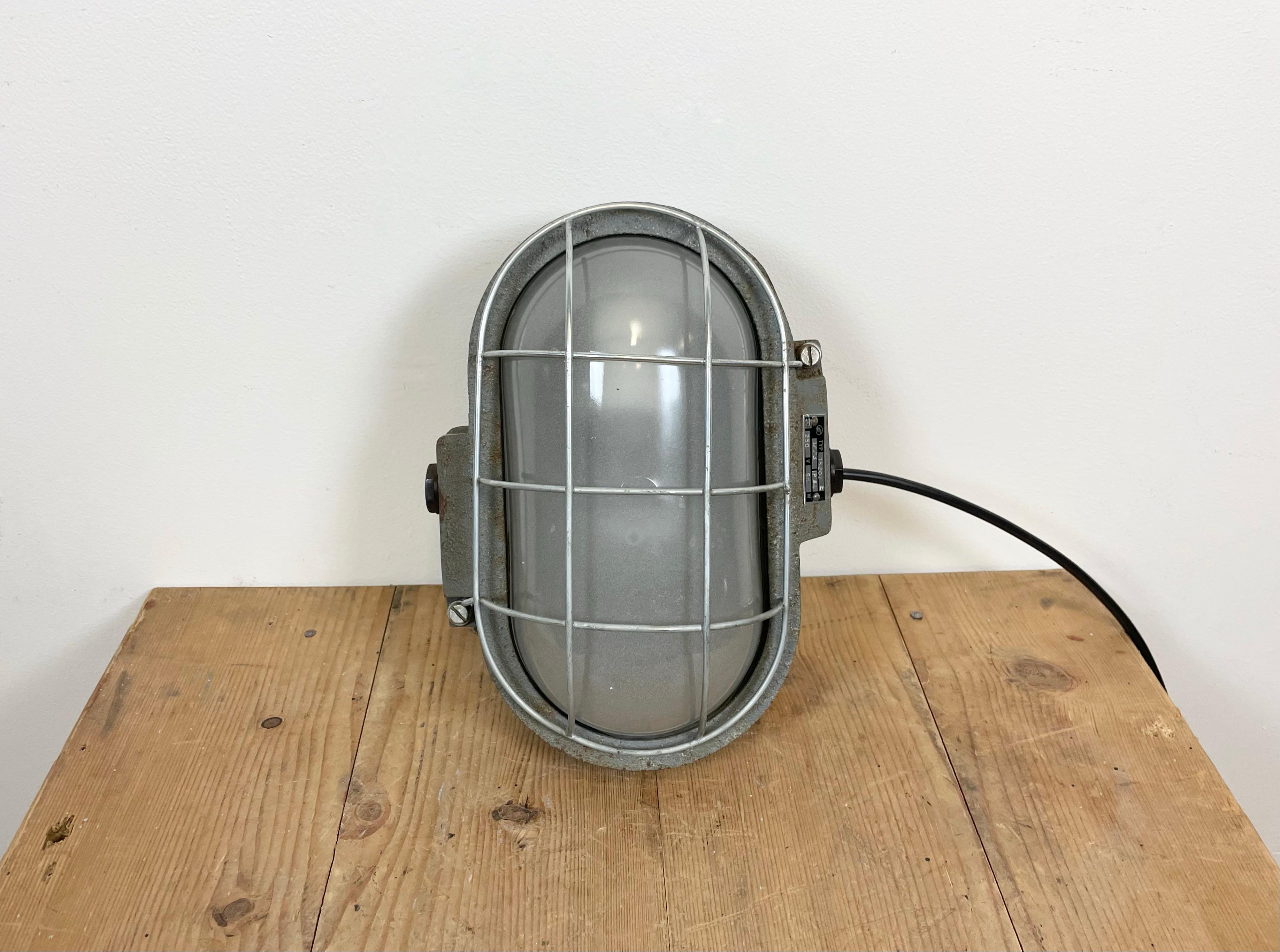 Industrial wall light made by Elektrosvit in former Czechoslovakia during the 1970s. It features a cast iron body, a milk glass cover and a steel grid.The porcelain socket requires E 27 lightbulbs. New wire. The weight of the lamp is 5 kg.