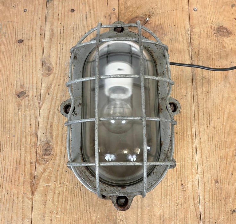 Industrial wall light made by Elektrosvit in former Czechoslovakia during the 1960s. It features a cast iron body, a clear glass cover and a steel grid.The porcelain socket requires E 27 light bulbs. New wire. The weight of the light is 6,5 kg.