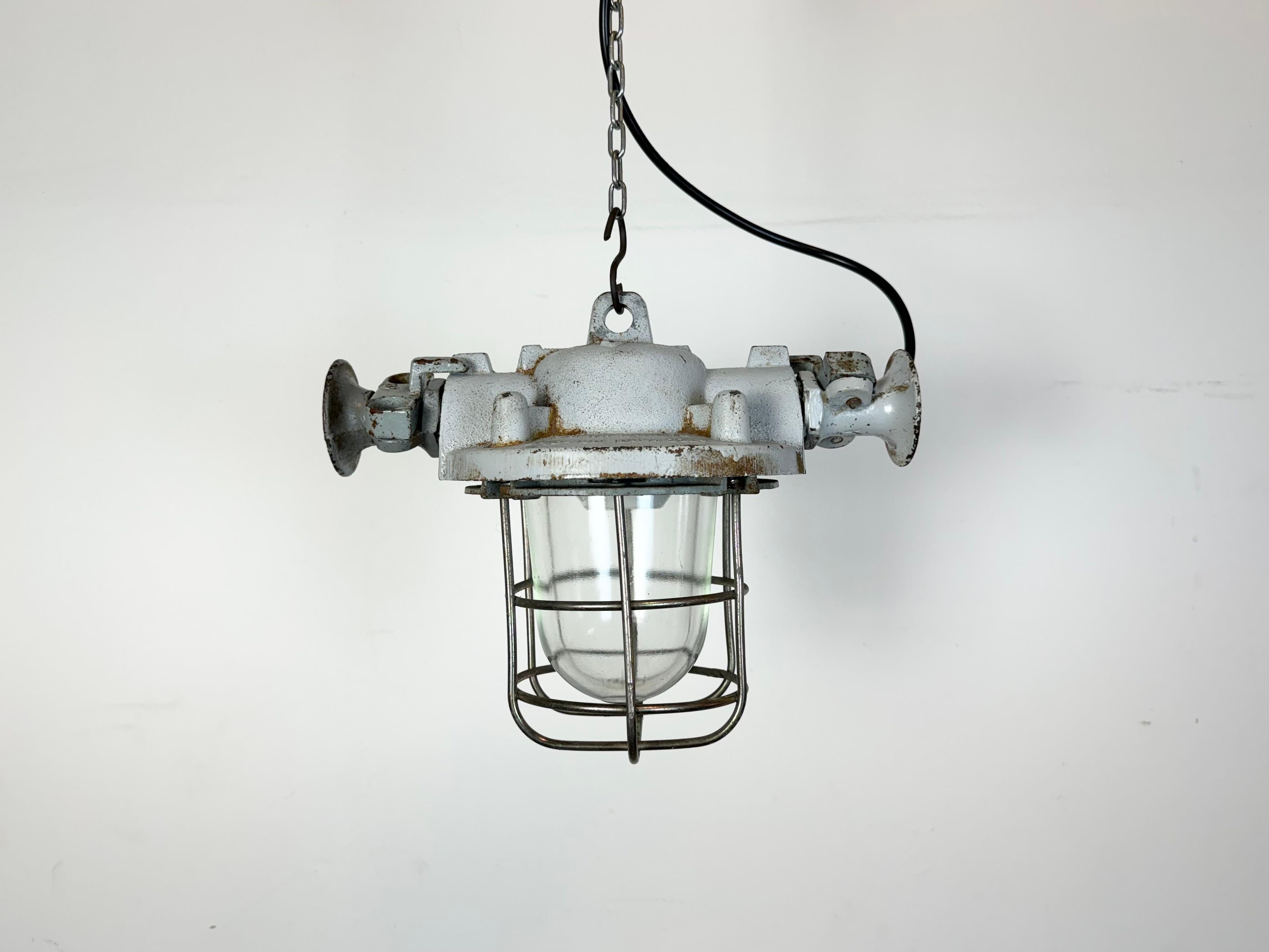 Esta luz industrial se fabricó en Polonia en la década de 1980. Tiene un cuerpo de fundición gris, una jaula de hierro y un cristal antideflagrante. El casquillo de porcelana requiere bombillas estándar E 27/ E26. Cable nuevo. El peso de la lámpara