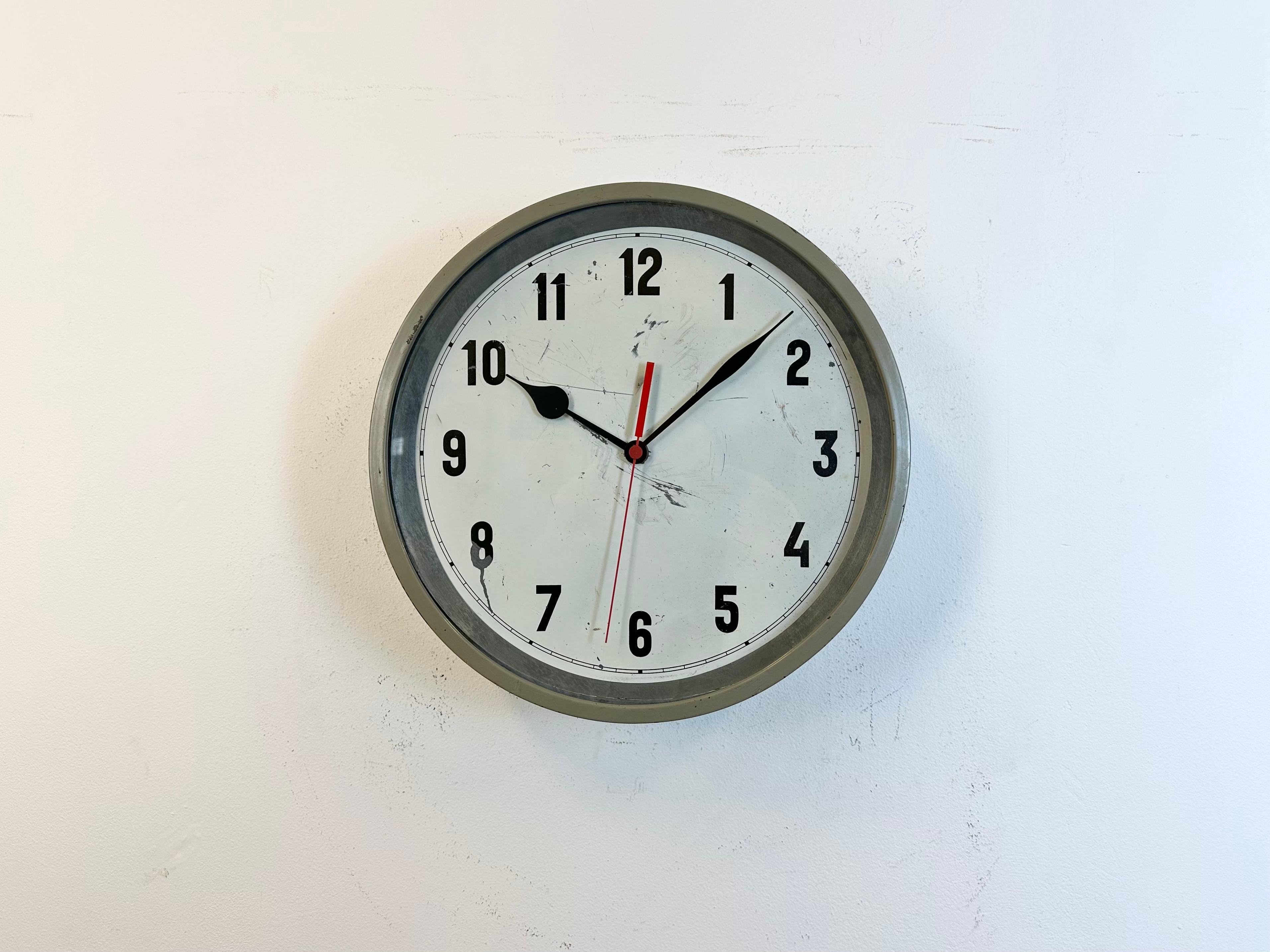 This factory wall clock was produced in former Czechoslovakia during the 1950s. It features a grey metal frame, iron dial, aluminum hands and clear glass cover. Former electrical slave clock has been converted into a battery-powered clockwork and