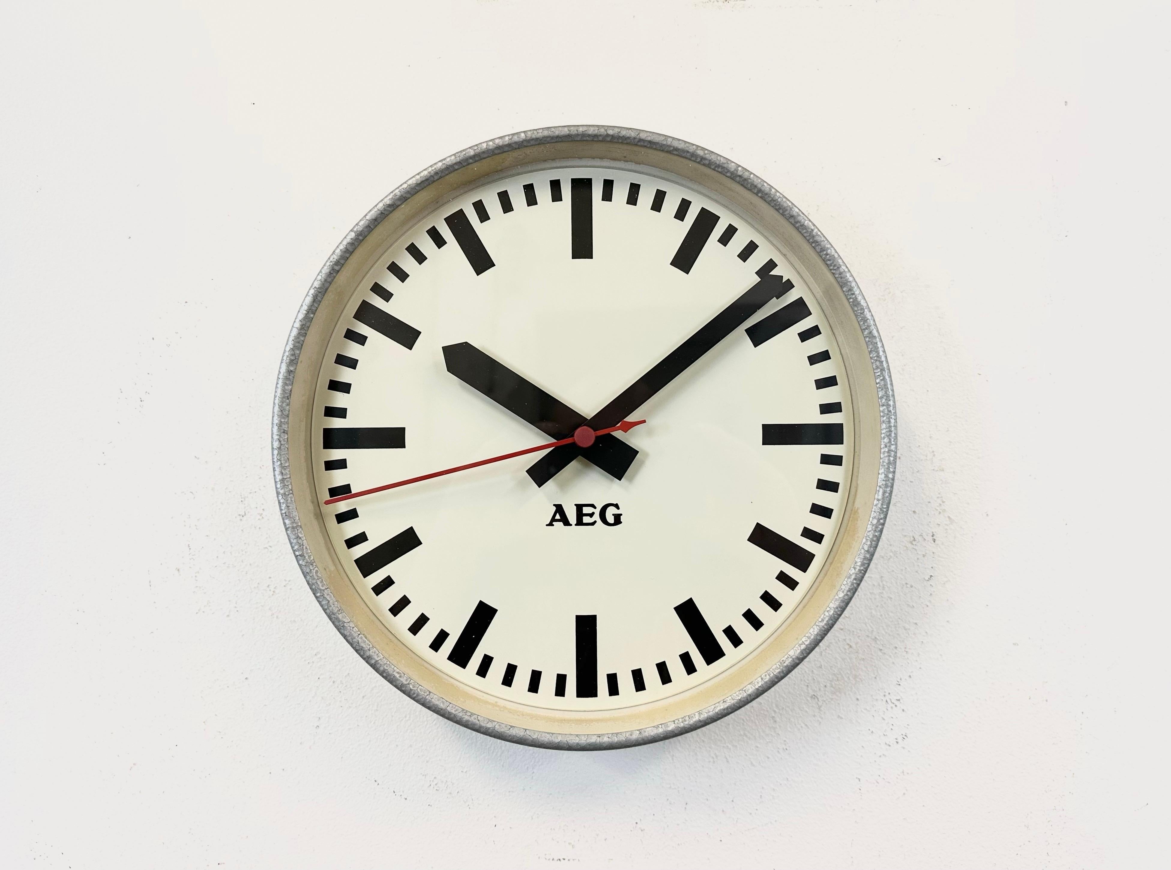 This wall clock was produced by AEG in Germany during the 1960s. It features a grey iron frame, a metal dial and a clear glass cover. The piece has been converted into a battery-powered clockwork and requires only one AA-battery. The weight of the