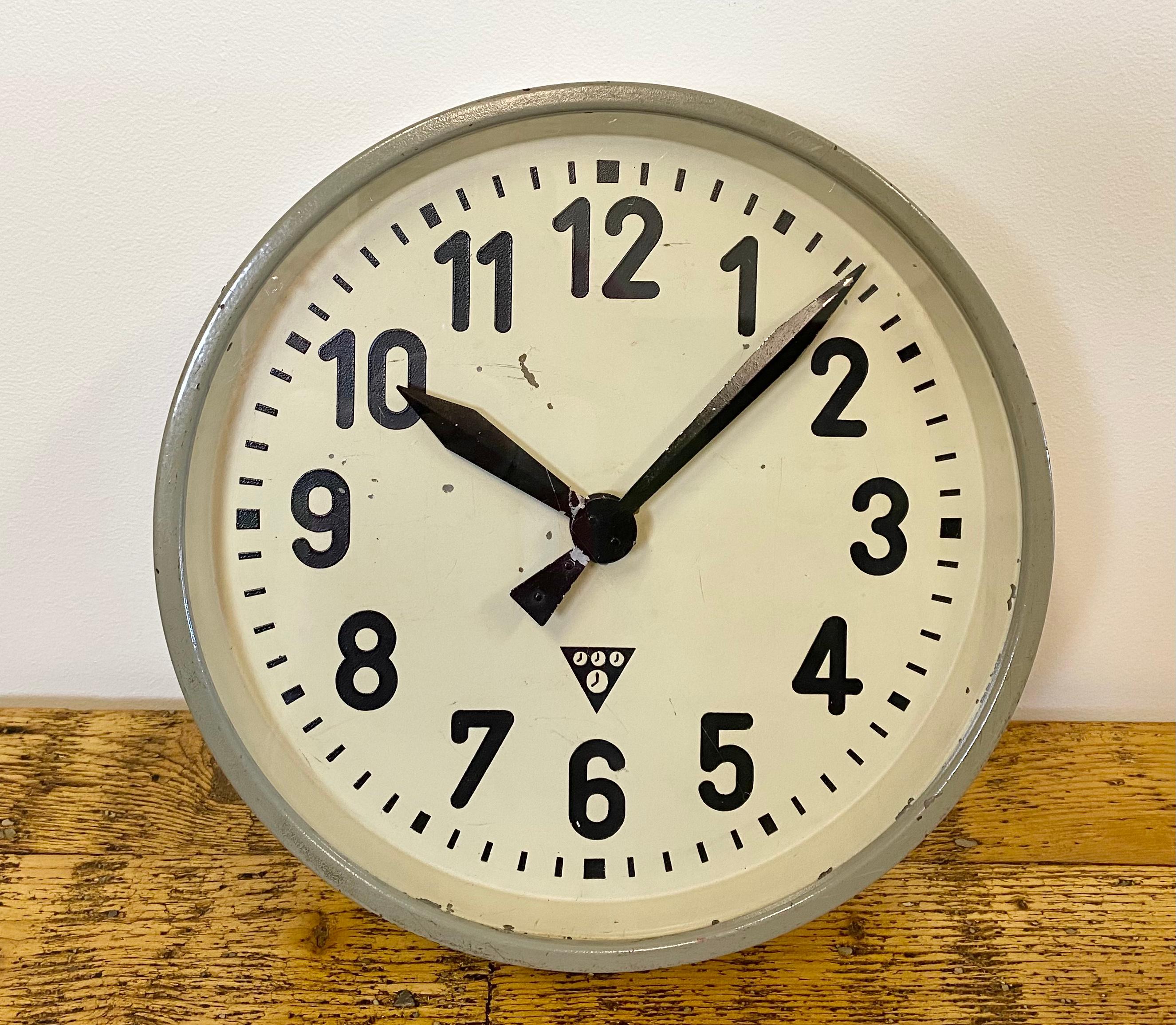 This wall clock was produced by Pragotron in former Czechoslovakia during the 1950s. It features a grey metal frame, iron dial, aluminium hands and a clear glass cover. The piece has been converted into a battery-powered clockwork and requires only
