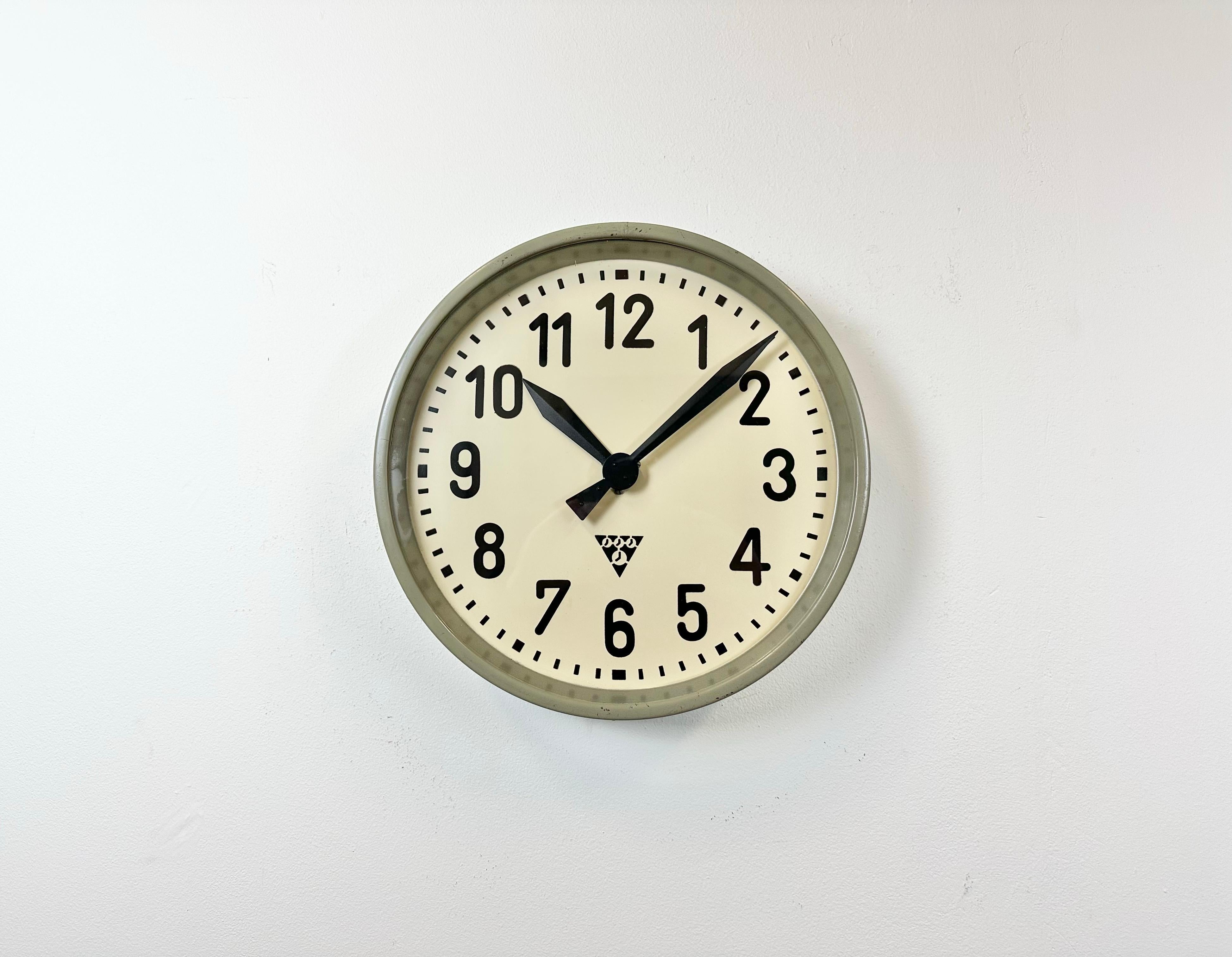 This wall clock was produced by Pragotron in former Czechoslovakia during the 1950s. It features a grey metal frame, iron dial, aluminium hands and a clear glass cover. The piece has been converted into a battery-powered clockwork and requires only