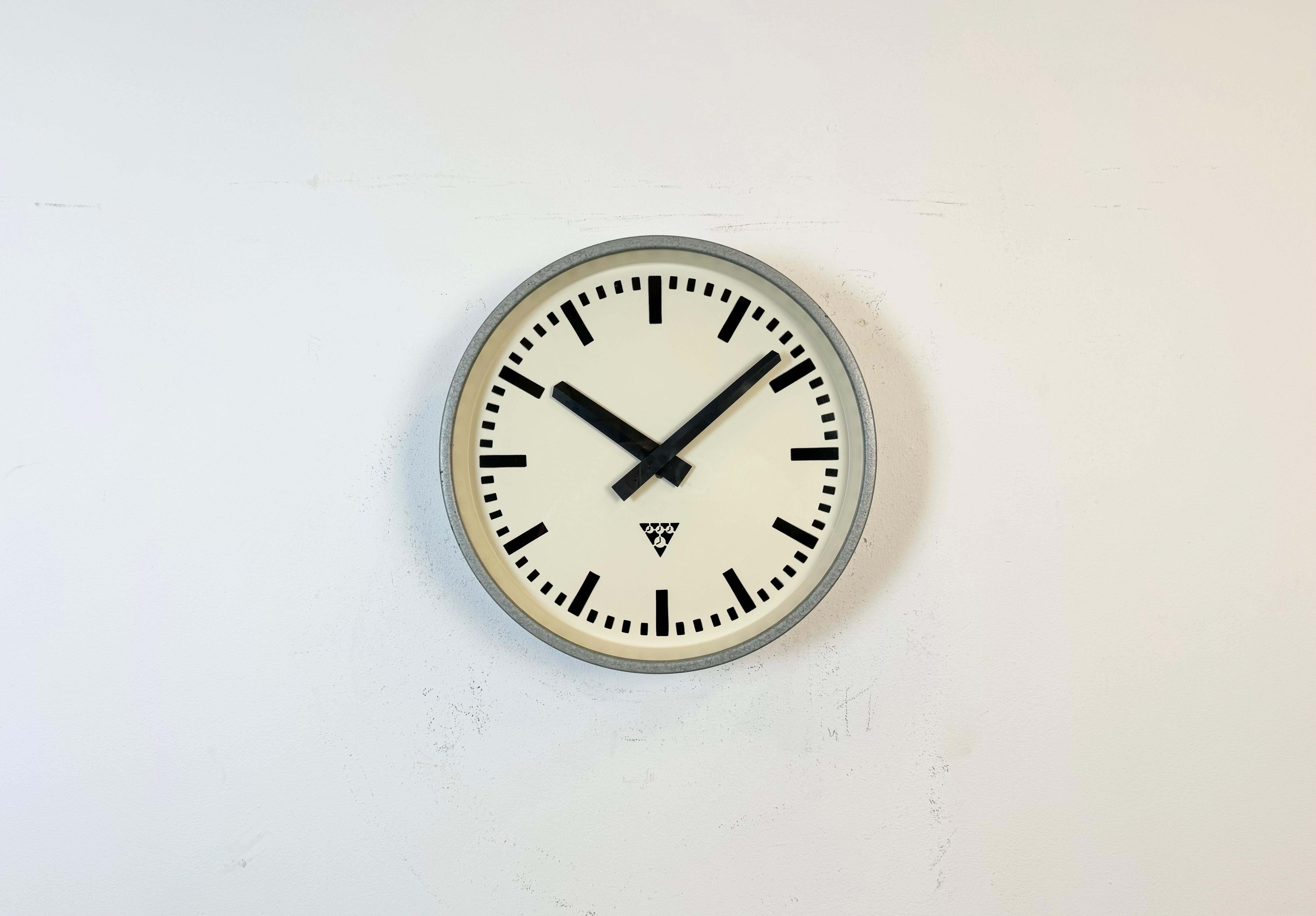 This wall clock was produced by Pragotron in former Czechoslovakia during the 1960s. It features a grey hammerpaint metal frame, an iron dial, an aluminium hands and a clear glass cover. Former factory electric slave clock has been converted into a
