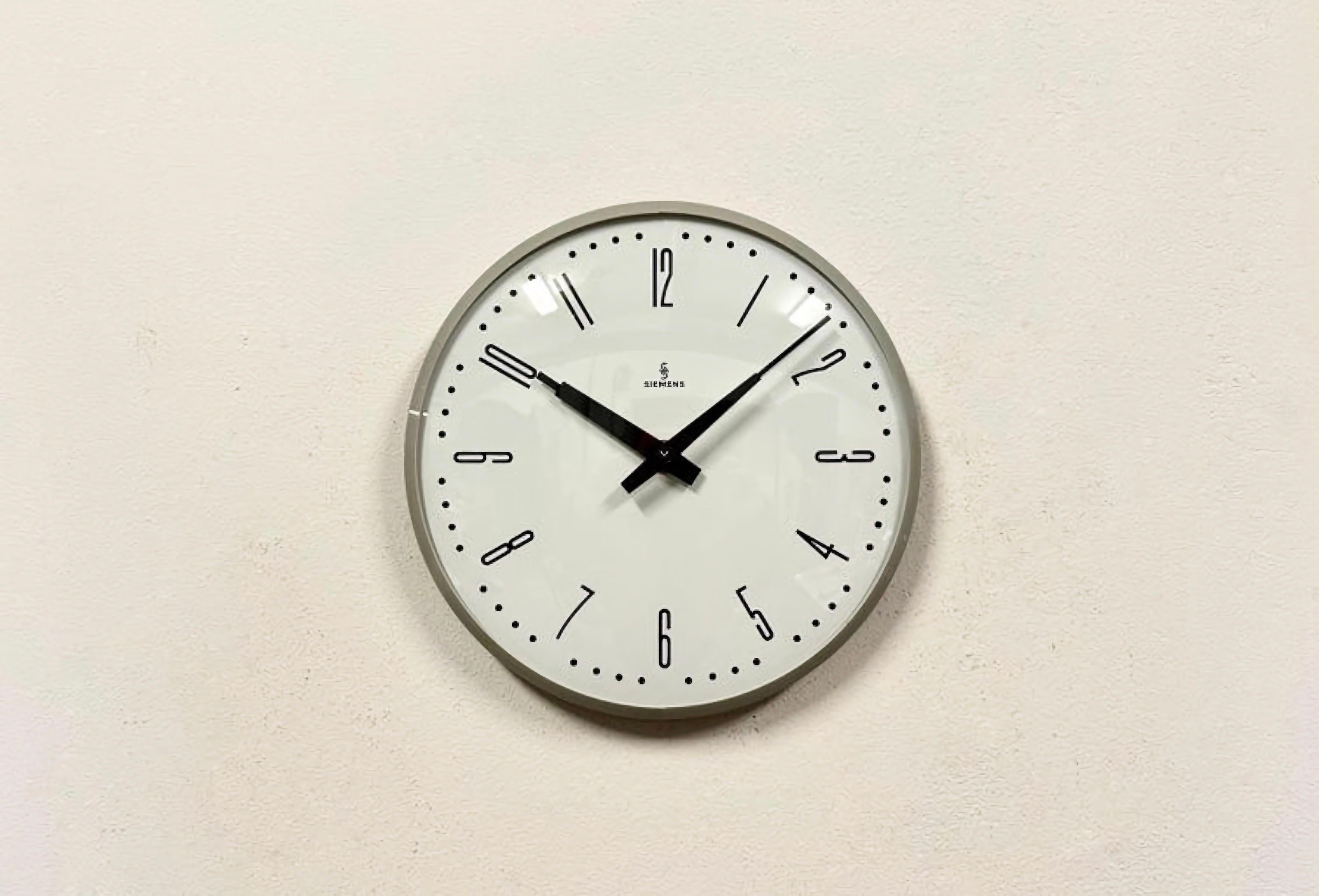 This wall clock was produced by Siemens in Germany during the 1970s. It features a grey bakelite frame, a metal dial and a convex clear glass cover. The piece has been converted into a battery-powered clockwork and requires only one AA-battery. The
