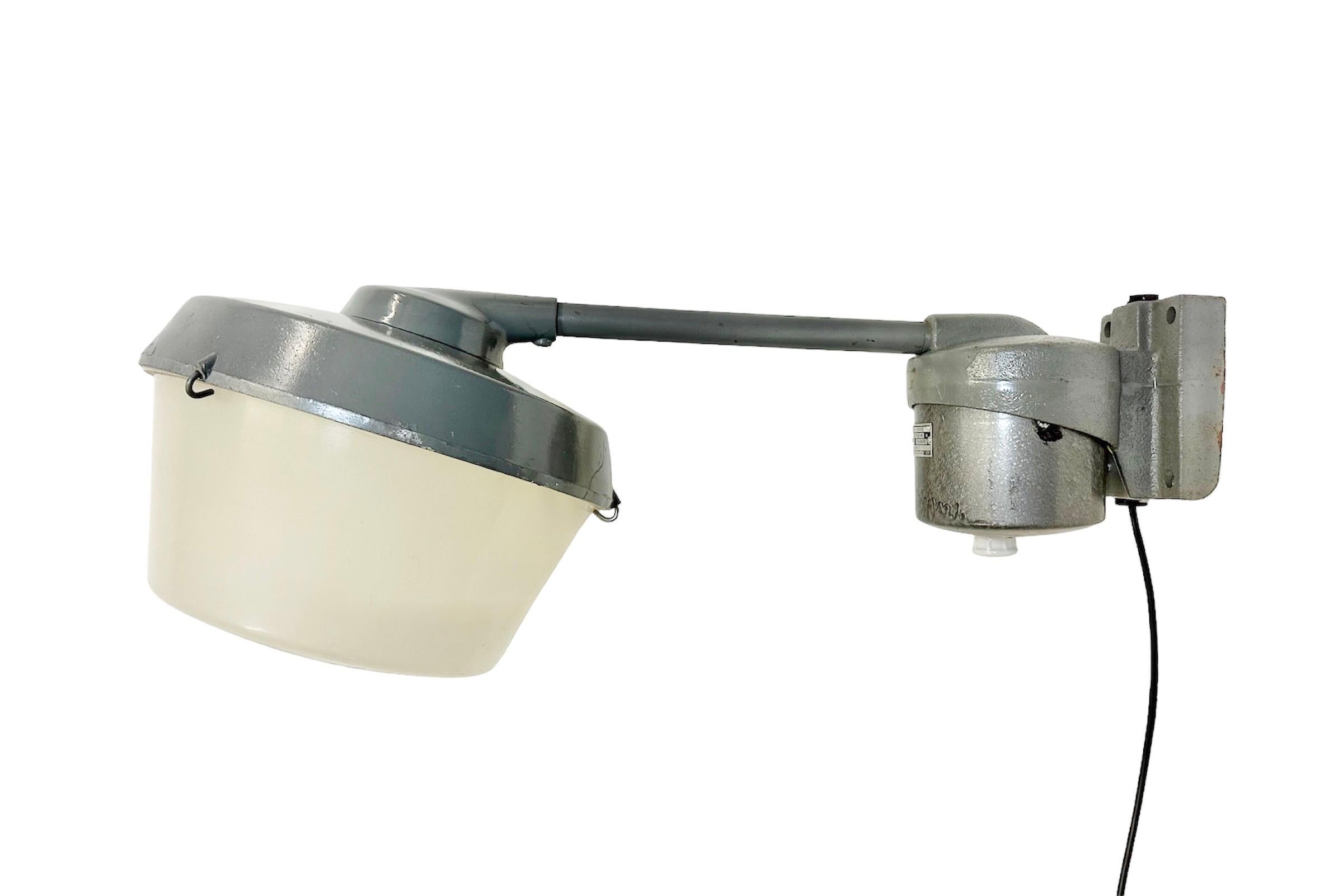 Industrial factory wall light made in former Czechoslovakia during the 1970s. It features a grey cast iron wall mounting and arm, a grey cast aluminium shade and a plastic milk glass cover.  The original socket requires standard E 27 / E 26 light
