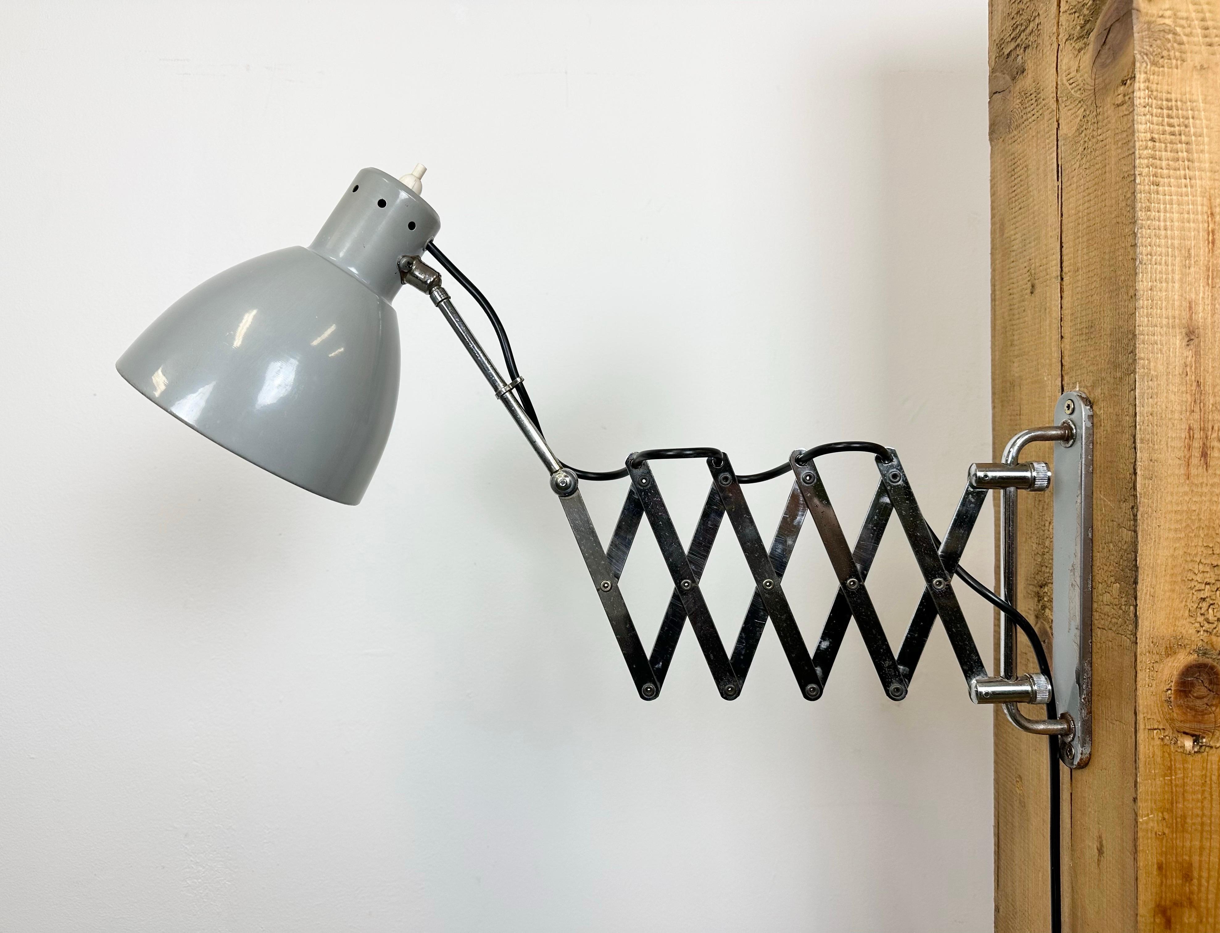 This vintage industrial grey scissor wall light was made in Italy during the 1960s. It features a grey metal shade with original switch and an iron chrome plated scissior arm and wall mounting. The scissor arm is extendable and can be turned