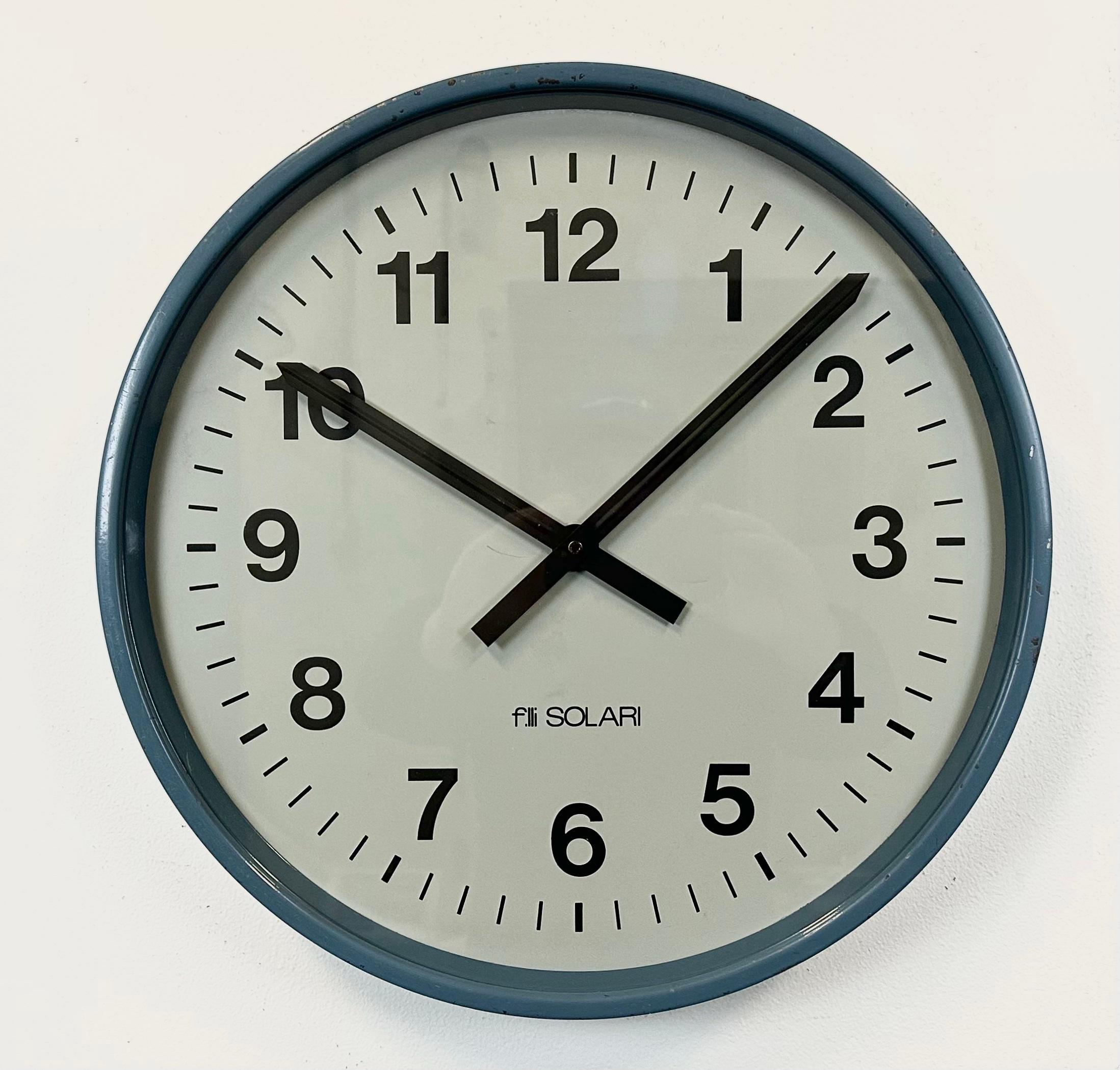 Questo orologio da parete è stato prodotto dalla Fratelli Solari Udine in Italia negli anni Settanta. Presenta una struttura in metallo blu, un quadrante in ferro, lancette in alluminio e un coperchio in vetro trasparente. Il pezzo è stato