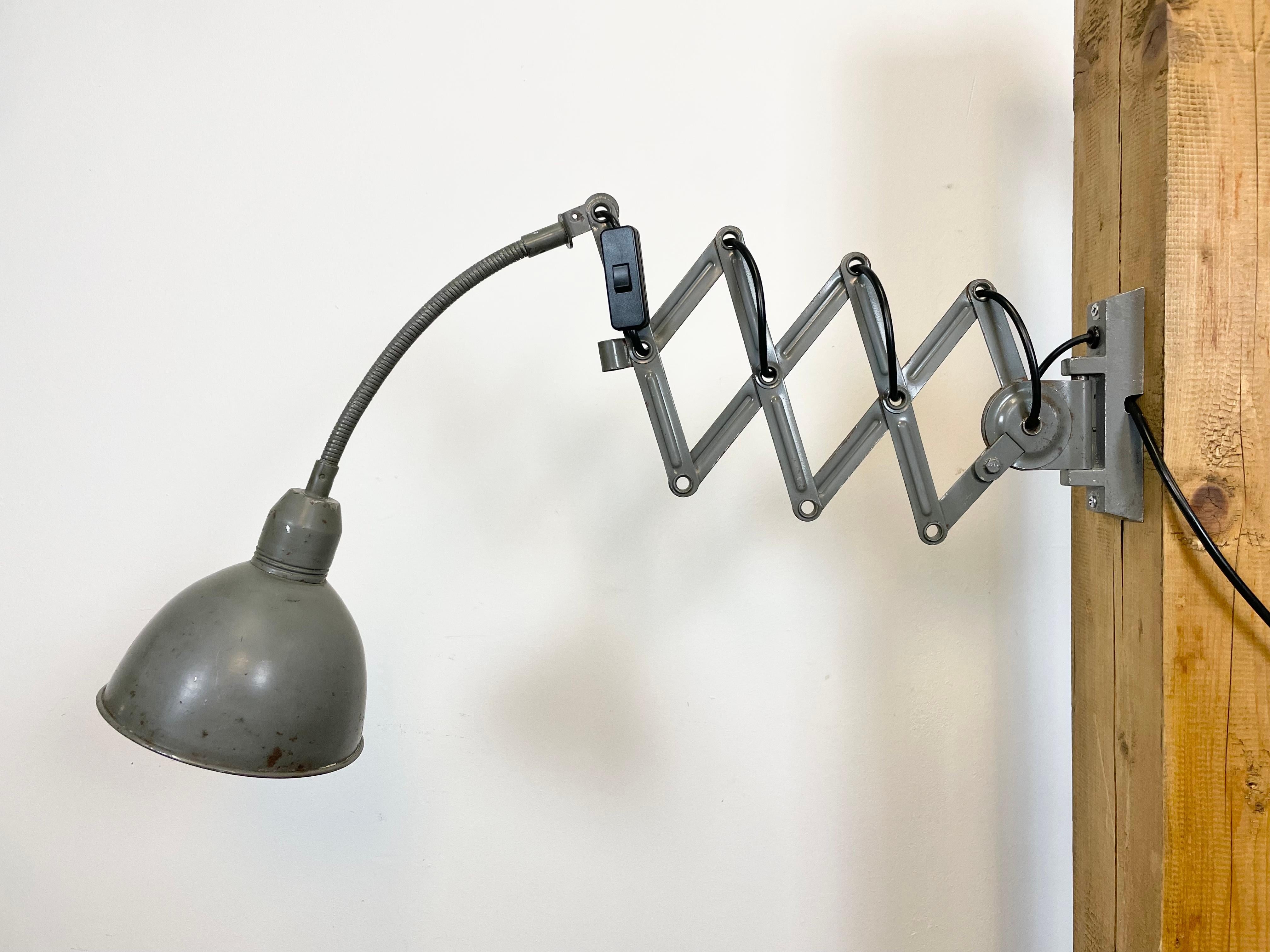 This grey vintage Industrial scissor wall lamp was produced by Elektroinstala in former Czechoslovakia during the 1960s. It has a metal lampshade. The iron scissor arm is extendable and can be turned sideways. The socket requires E 27 lightbulbs .