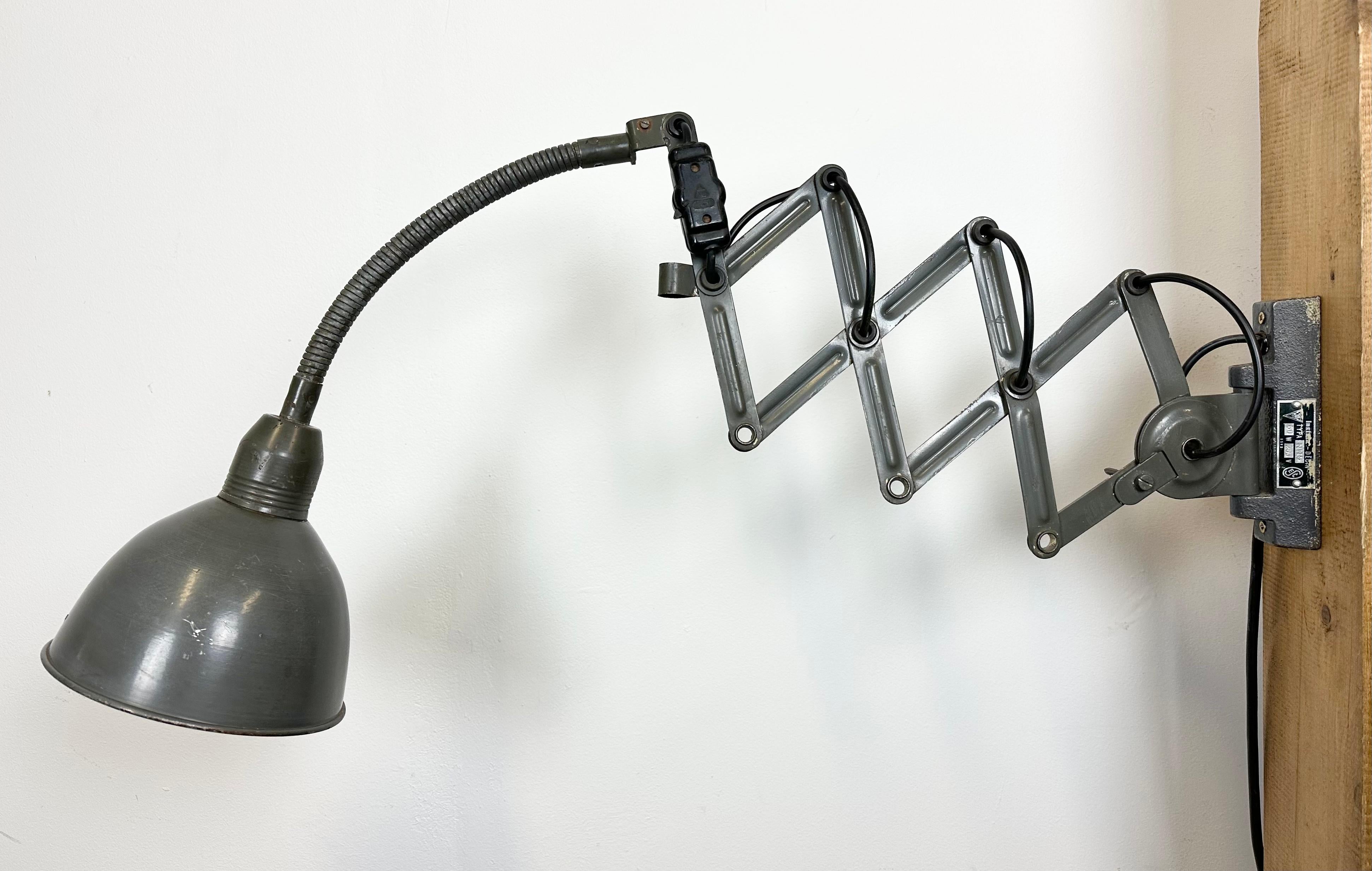 This vintage industrial grey scissor wall light was produced by Elektroinstala Decín in former Czechoslovakia during the 1960s. It has a metal lampshade. The iron scissor arm is extendable and can be turned sideways. The socket requires E 27/ E26