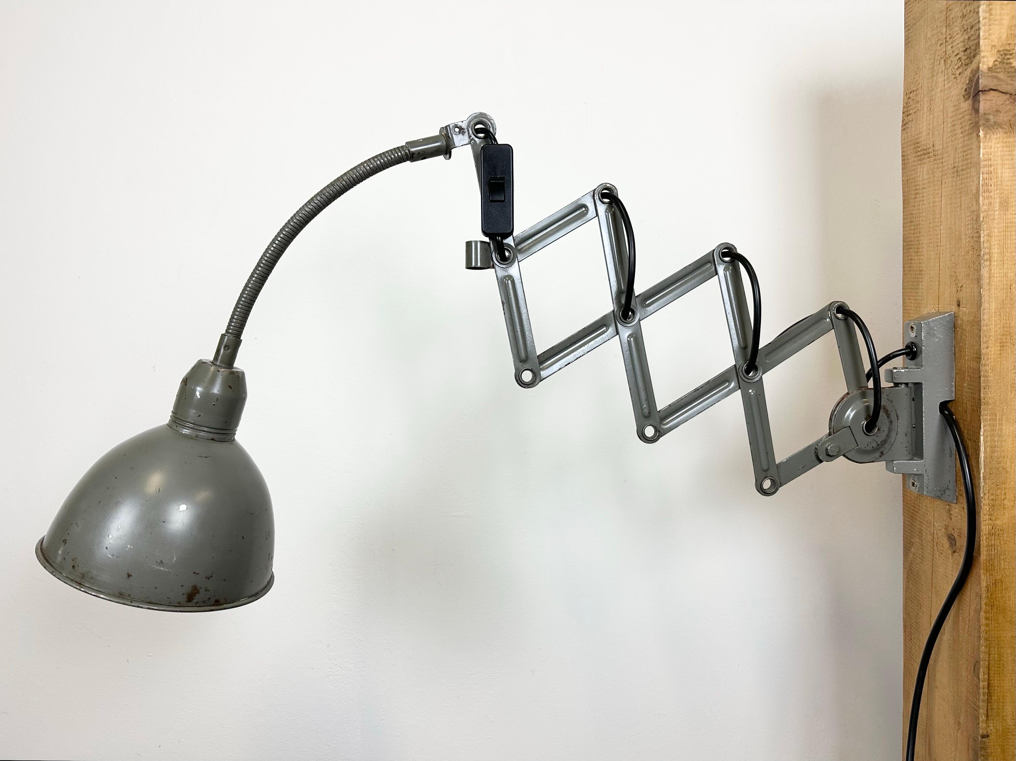 This vintage Industrial grey scissor wall light was produced by Elektroinstala Decín in former Czechoslovakia during the 1960s. It has a metal lampshade. The iron scissor arm is extendable and can be turned sideways. The socket requires E 27/ E26
