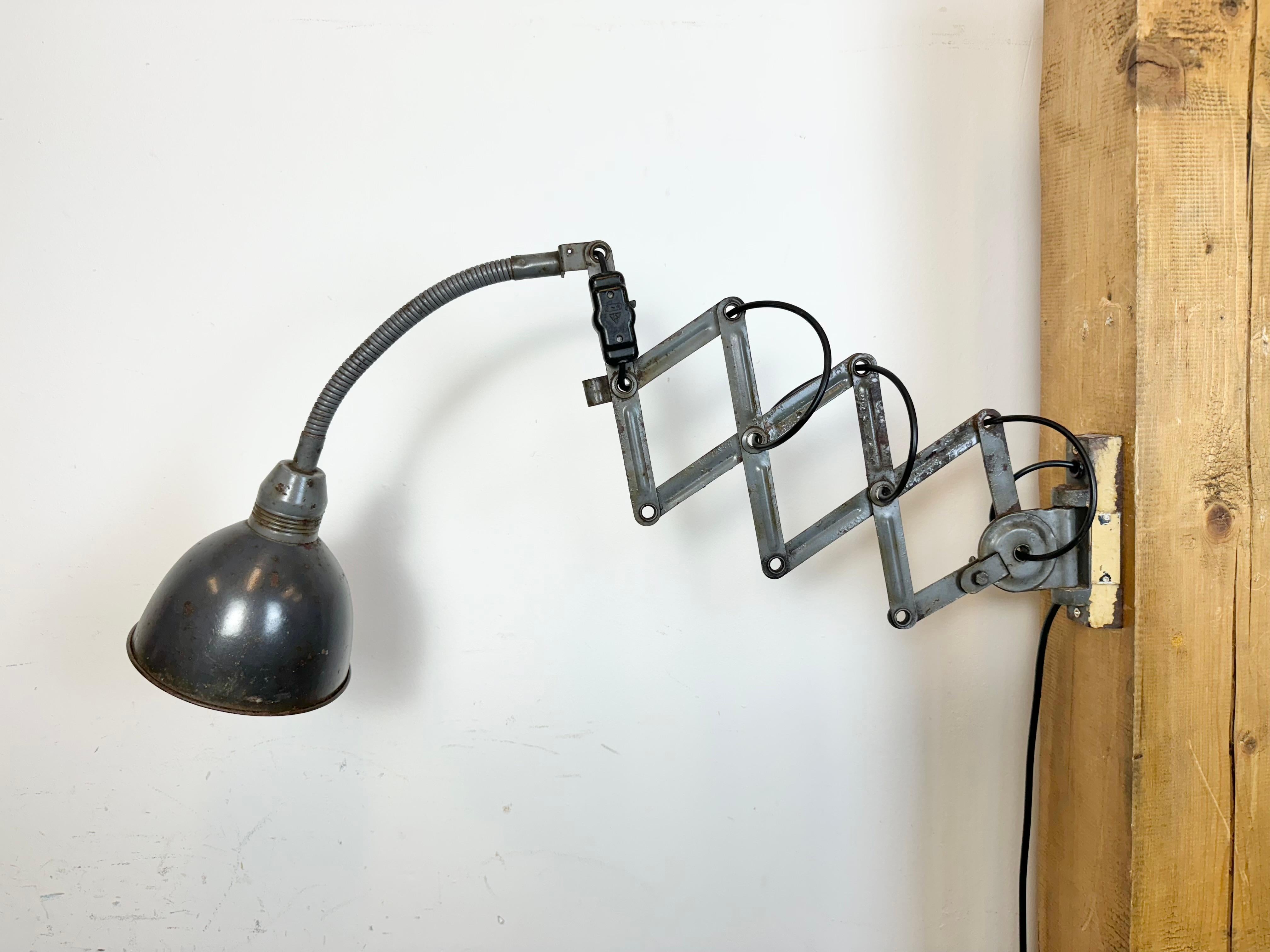 Questa lampada da parete a forbice vintage di colore grigio industriale è stata prodotta da Elektroinstala Decín nell'ex Cecoslovacchia negli anni '60. Ha un paralume in metallo. Il braccio a forbice in ferro è estensibile e può essere girato