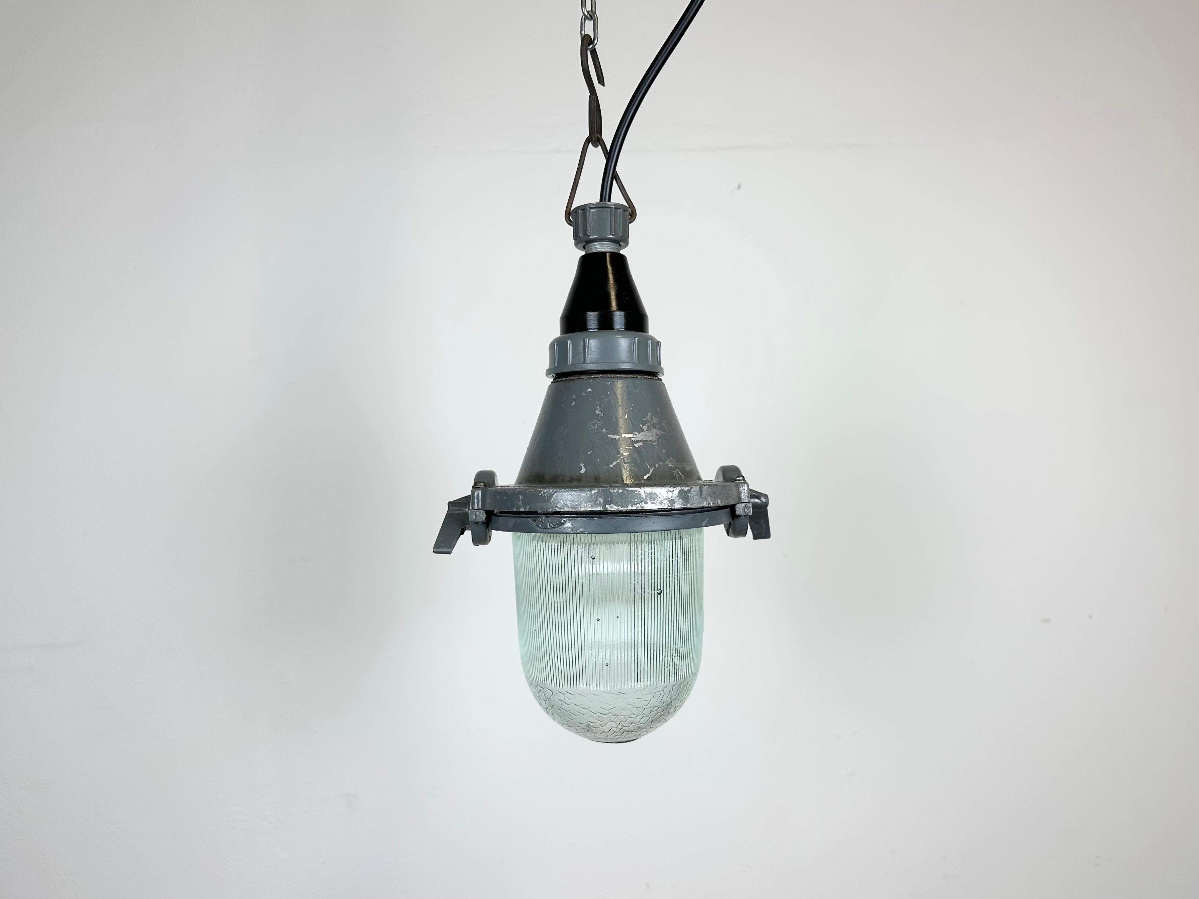 Lampada industriale grigia con lampadina in vetro protettivo massiccio. Prodotto nell'ex Unione Sovietica negli anni '60. Presenta un corpo in alluminio fuso con piano in bachelite e coperchio in vetro trasparente. La presa richiede lampadine E27.