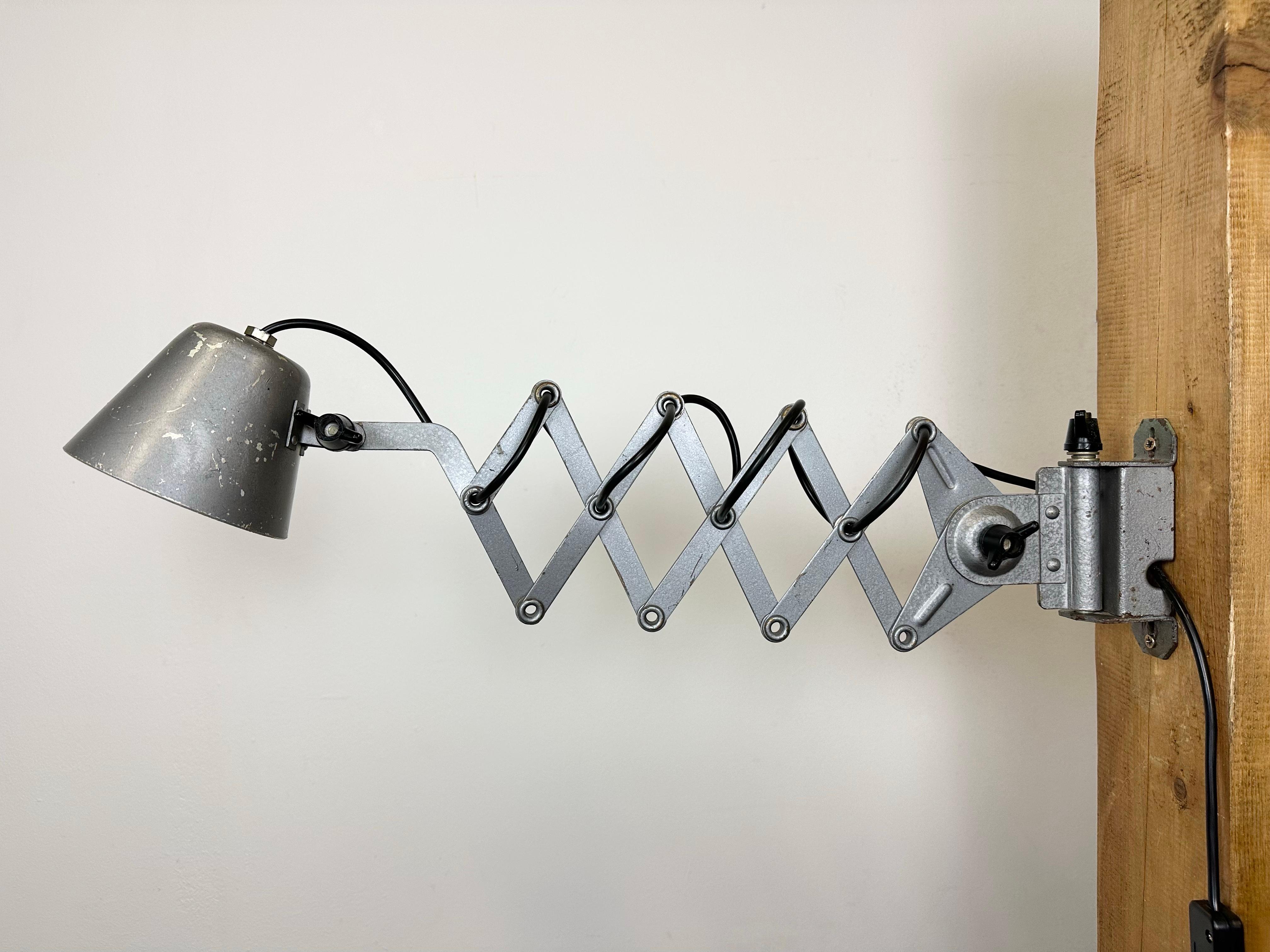 This vintage industrial grey scissor wall light was made in former Soviet Union during the 1960s. It features a grey metal shade and iron hammerpaint arm. The scissor arm is extendable and can be turned sideways. The socket requires E 14 light bulbs