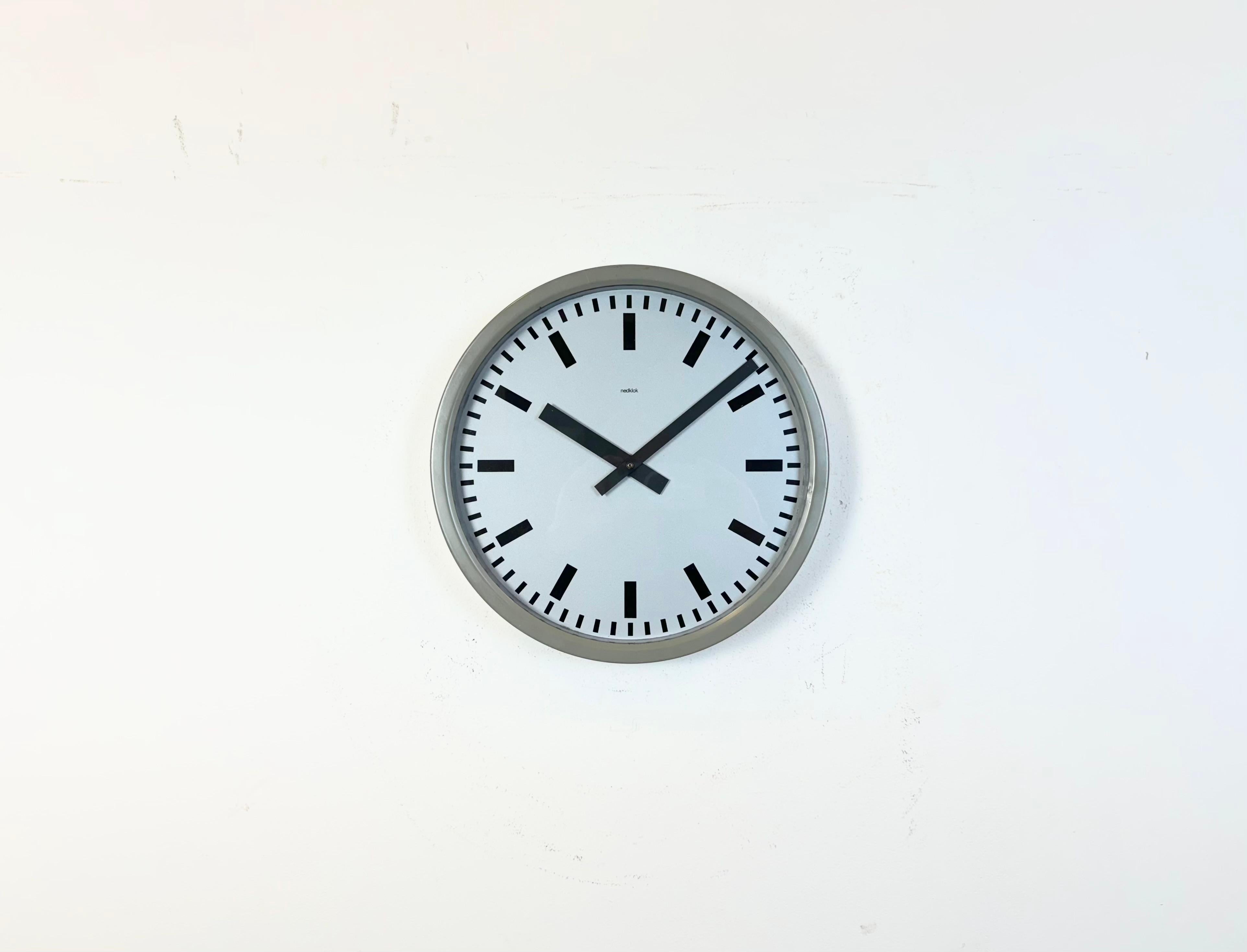 El reloj de pared Nedklok se fabricó en Holanda durante la década de 1960. Presenta un marco de hierro gris, una esfera metálica, agujas de aluminio y tapa de cristal transparente. La pieza se ha convertido en un mecanismo de relojería que funciona