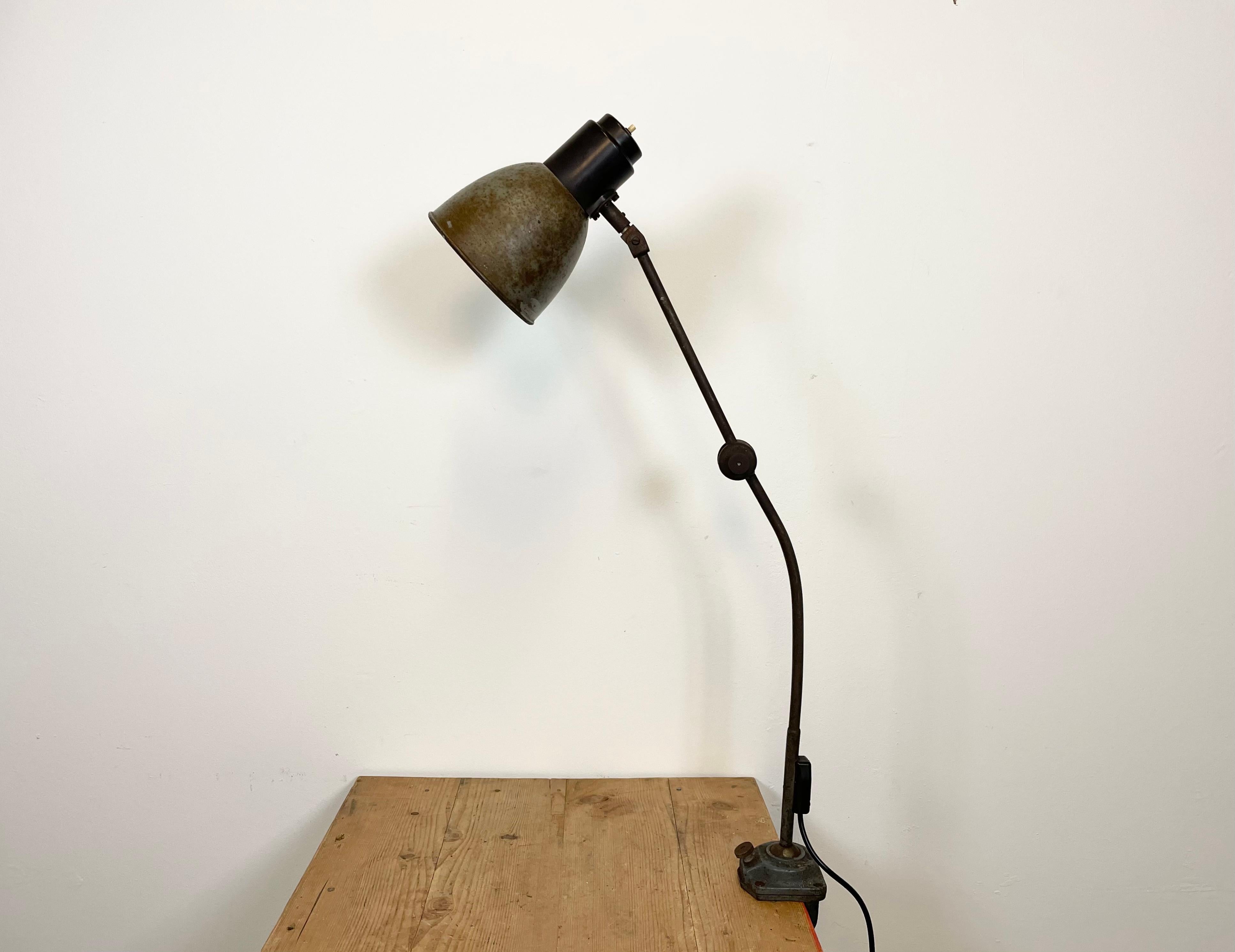 Industrial table lamp from the 1950s. It features an iron clamp base, an iron arm with three adjustable joints and metal shade with bakelite top. The switch is situated directly on the top. The socket requires E 27 lightbulb. New wiring.