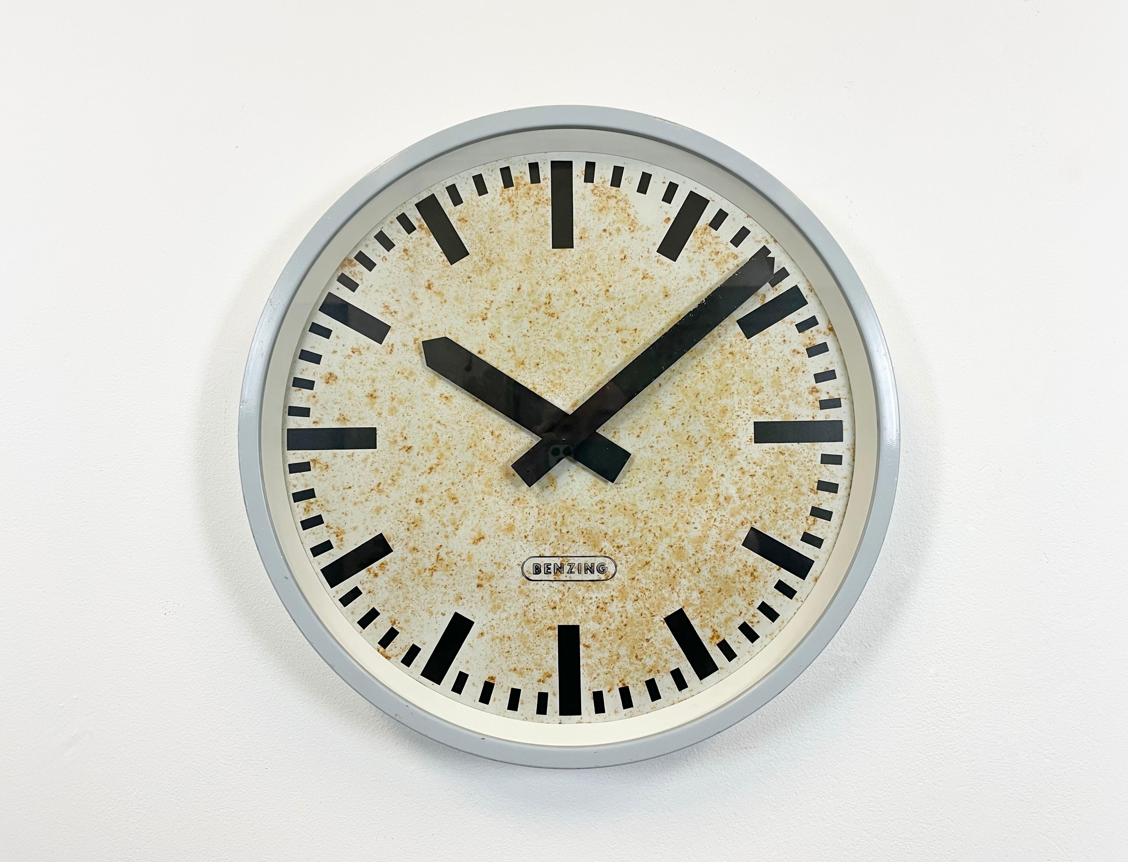 Benzing wall clock was made in Germany during the 1960s. It features a grey iron frame, a metal dial, an aluminium hands and clear glass cover. The piece has been converted into a battery-powered clockwork and requires only one AA-battery. The