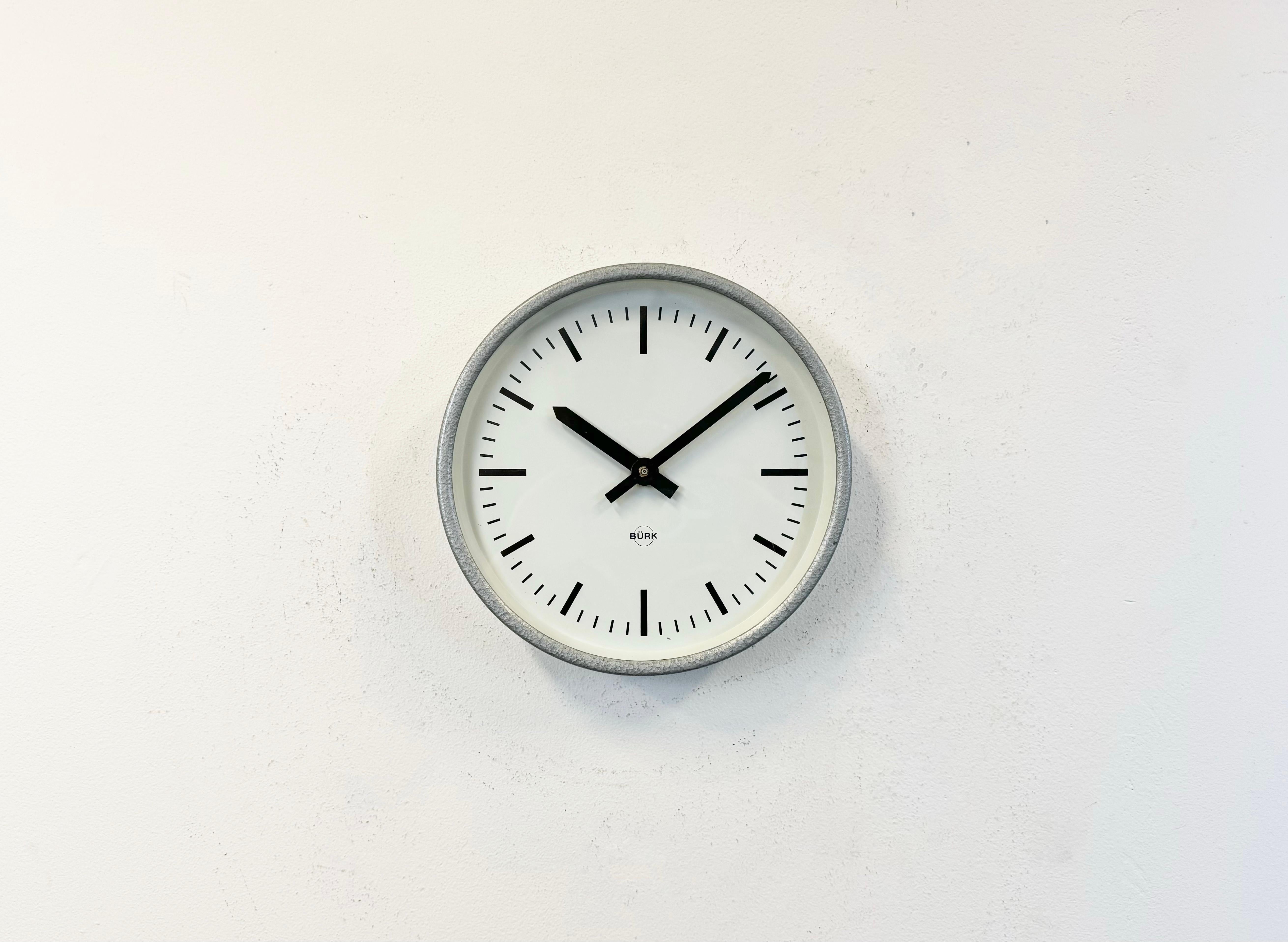 L'horloge murale Burk a été fabriquée en Allemagne de l'Ouest dans les années 1970. Elle se compose d'un cadre en fer gris, d'un cadran en métal, d'aiguilles en aluminium et d'un couvercle en verre transparent. La pièce a été convertie en un