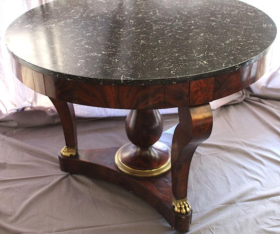 A beautiful and good sized centre pedestal table with a grey marble top and gilt claw feet detail and gilded bronze detail on the base of the pedestal. Empire style dating from, circa 1840. Mahogany. On wheels.