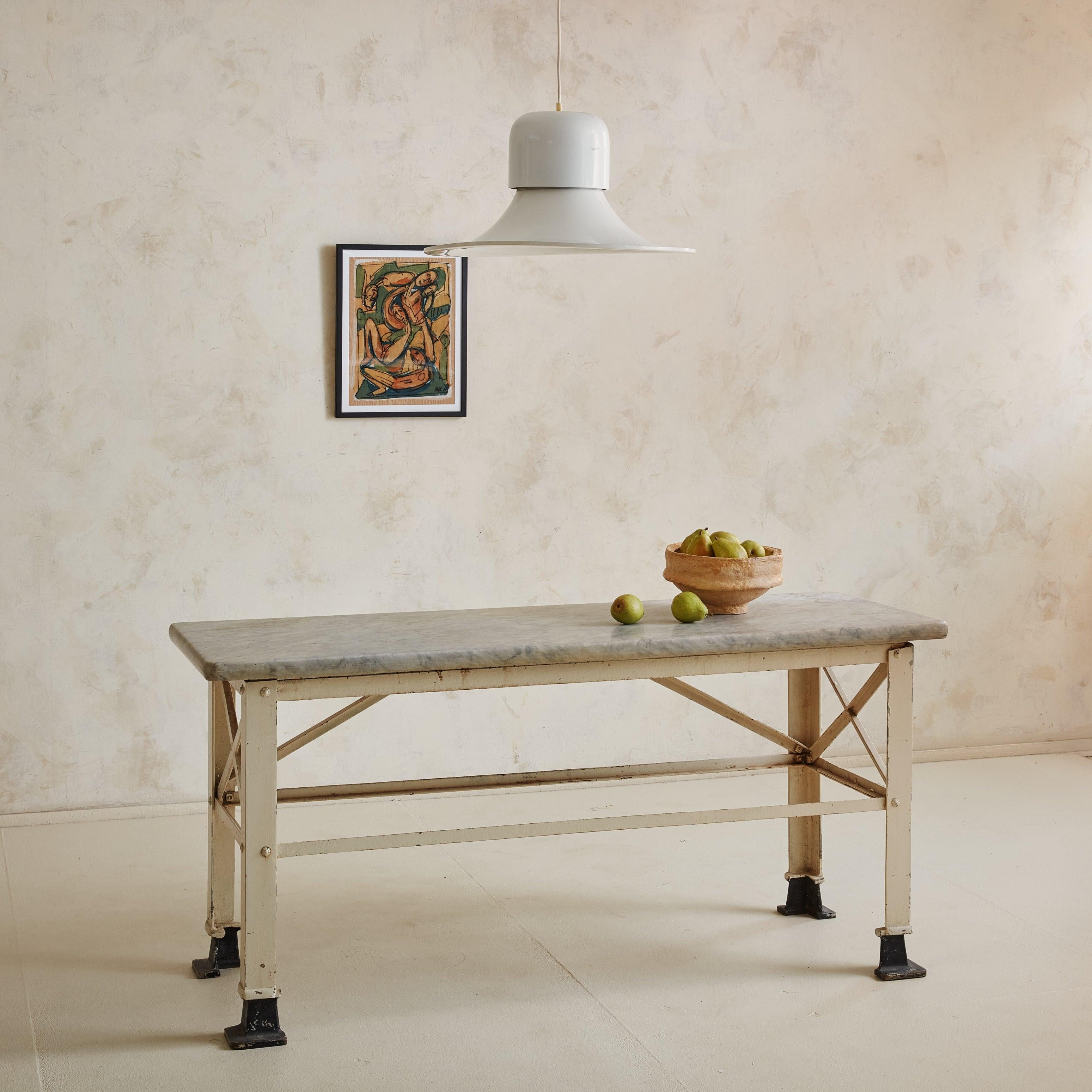 An Early 20th Century Italian kitchen island featuring a honed marble tabletop with a bullnose edge and gorgeous dove grey veining. The natural stone rests upon an Industrial metal base with ‘X’ side stretchers and a cream painted finish. Four