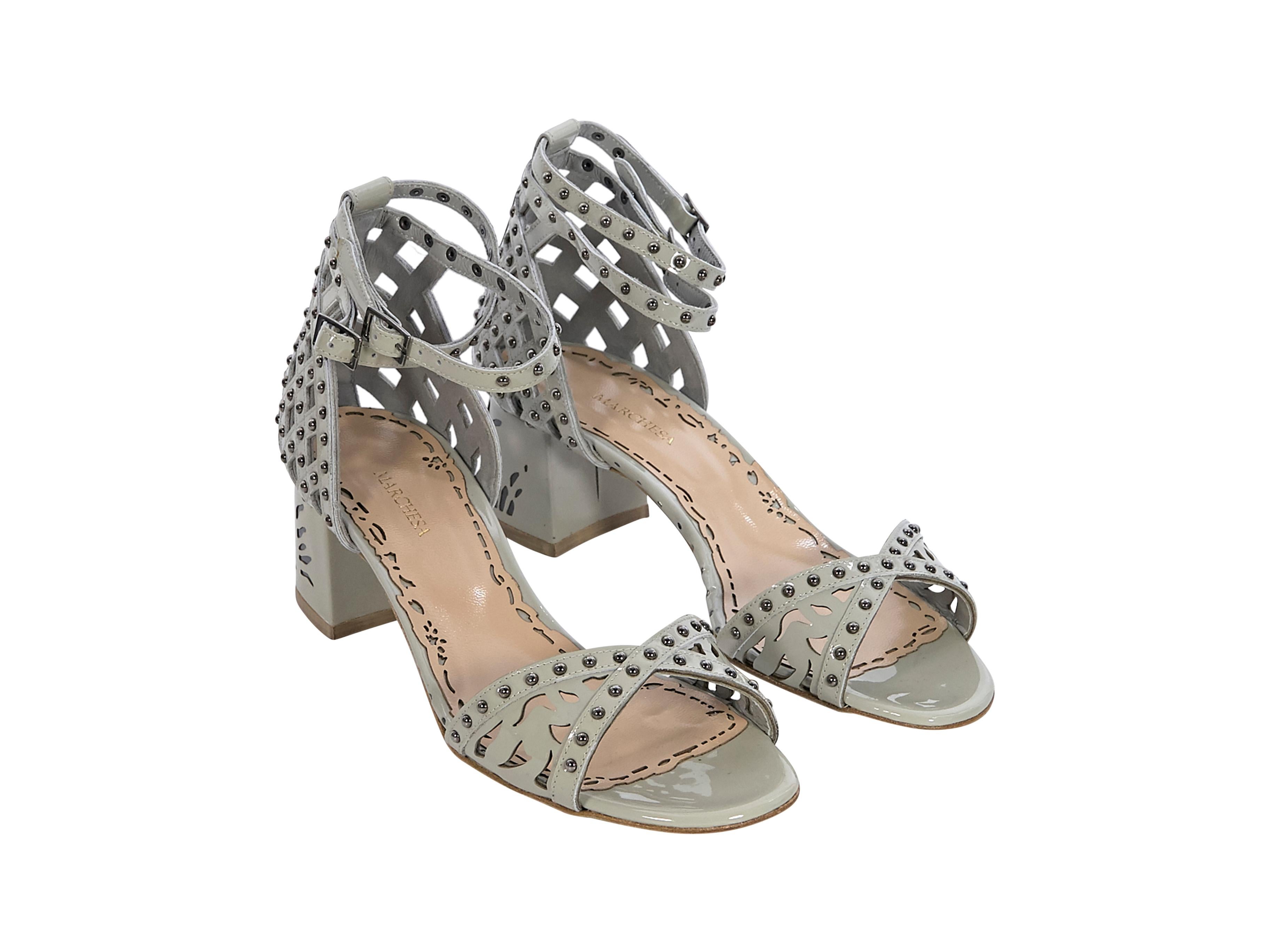 Product details:  Grey patent leather Kelly sandals by Marchesa. Silver-tone stud embellishments. Laser-cut out accents. Criss-cross straps at vamps. Adjustable buckle ankle strap closure. Pair with a ruffled mini dress.  2