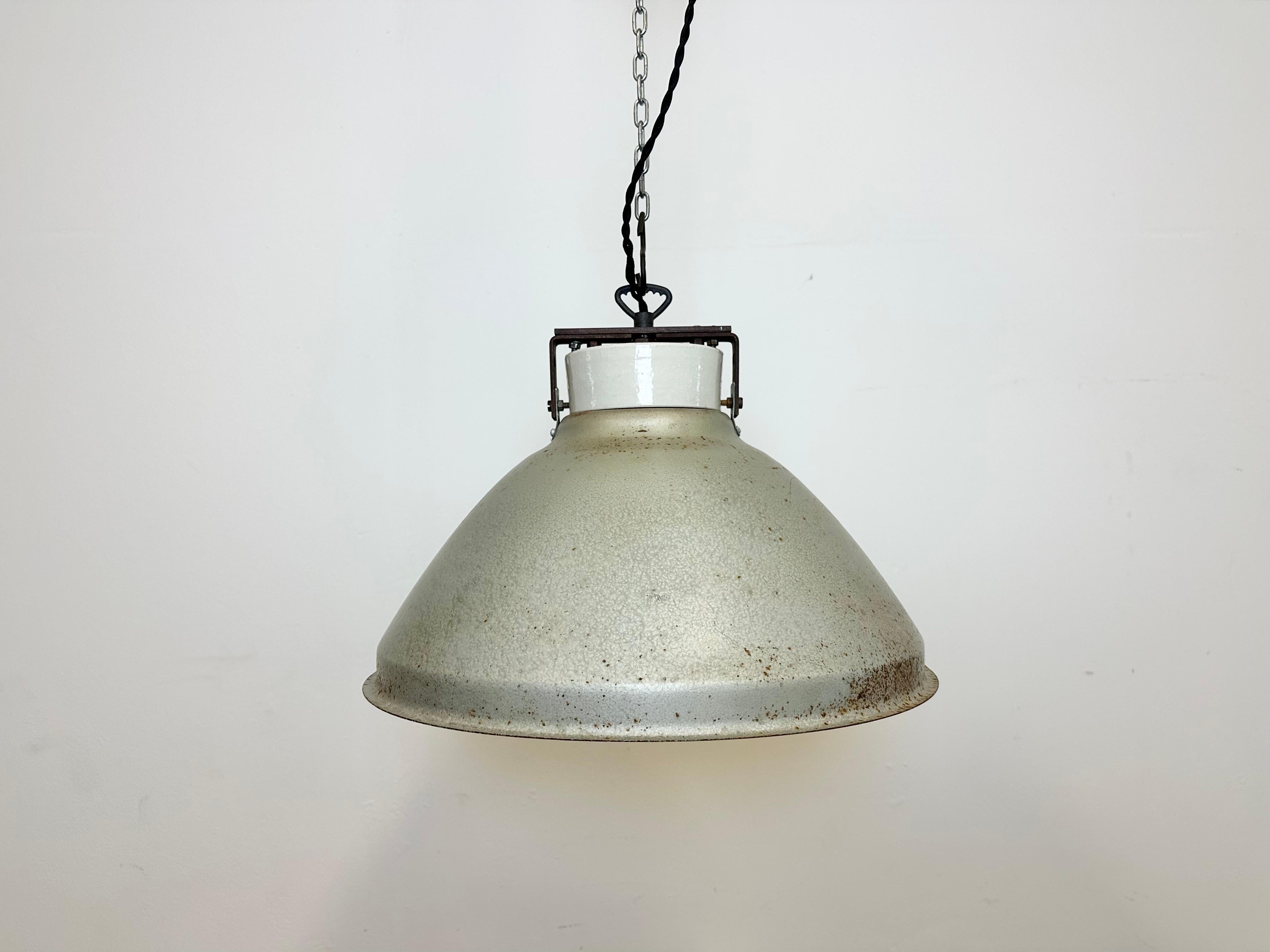 Industrial factory light made in Poland during the 1960s. It features grey metal shade with white interior and porcelain top with iron hook. The original socket requires standard E 27 / E 26 light bulbs. New textile wire. The diameter of the shade