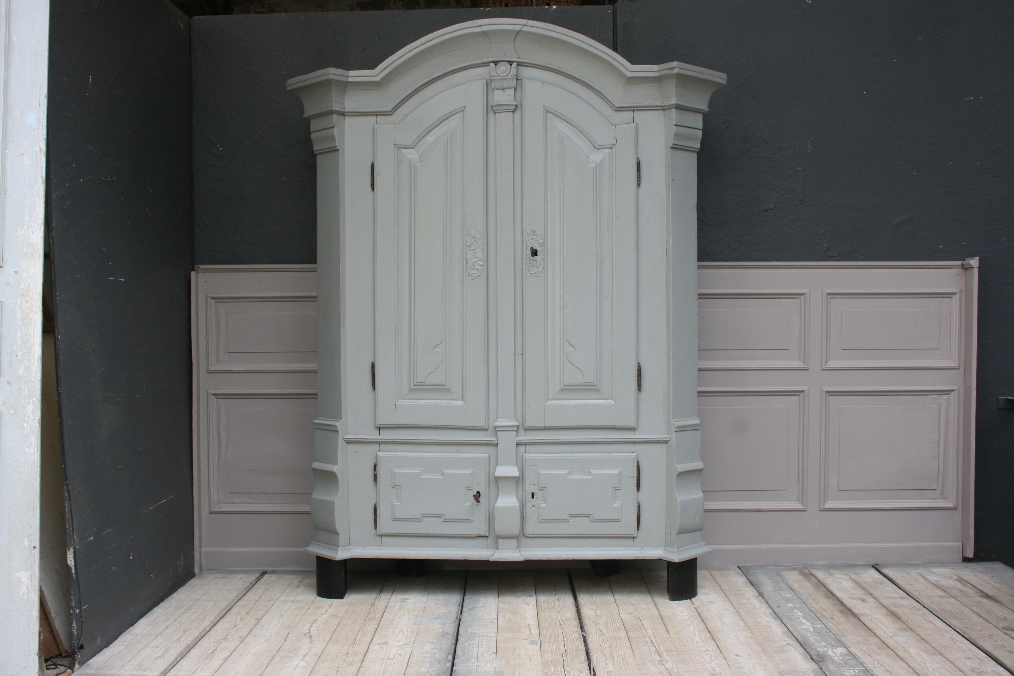 Antique South German (presumably Munich) baroque armoire from the 18th century made of pinewood.
Standing on 4 over-the-cornered ebonised feet with an arched cornice and cranked bevelled corners. High pedestal with 2 doors instead of drawers with