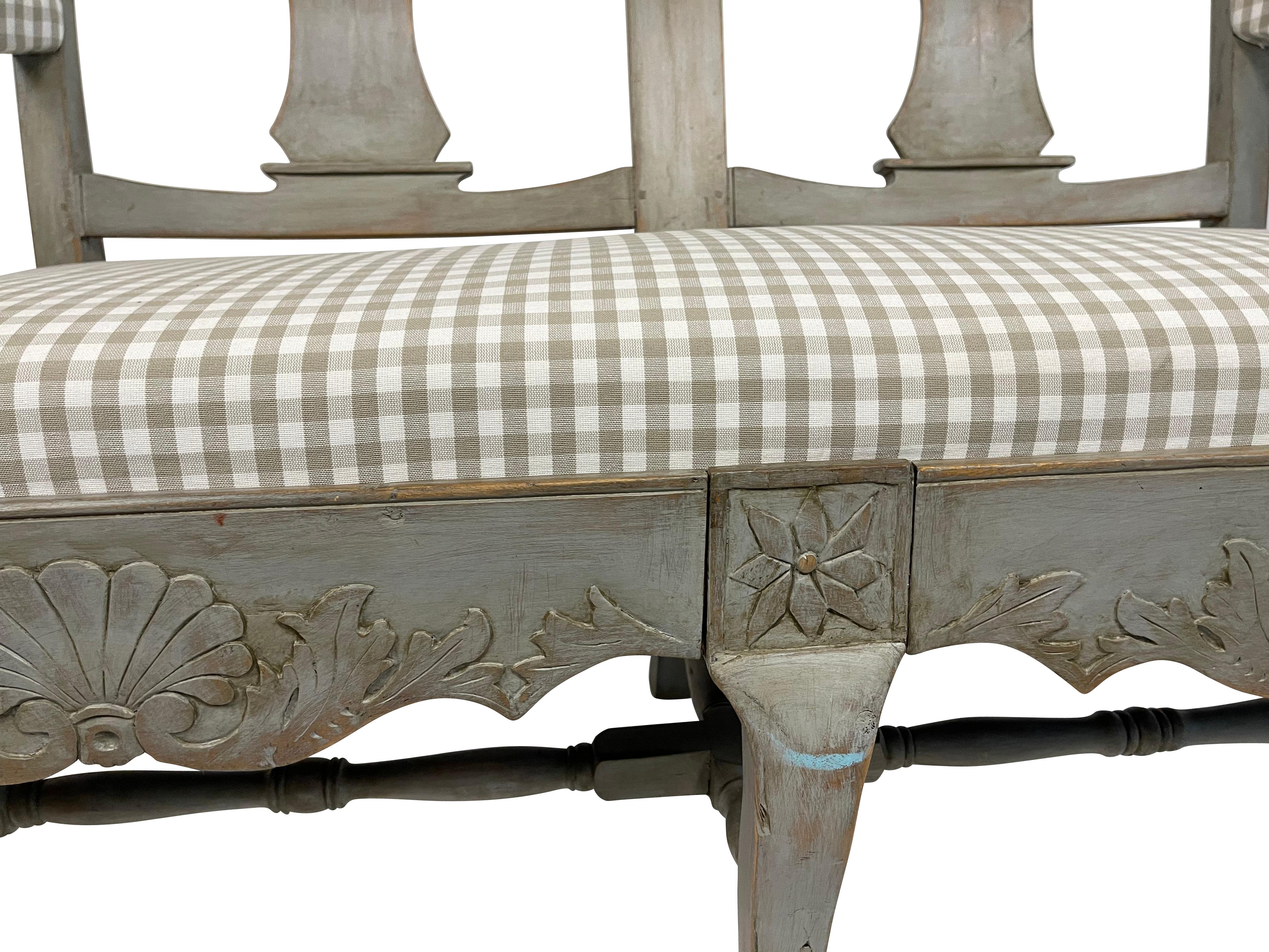 Swedish Gustavian rey painted settee with shell and foliate carving with turned stretcher bottom and gently curved legs. Newly upholstered in grey and white gingham seat cover. Measures: 44