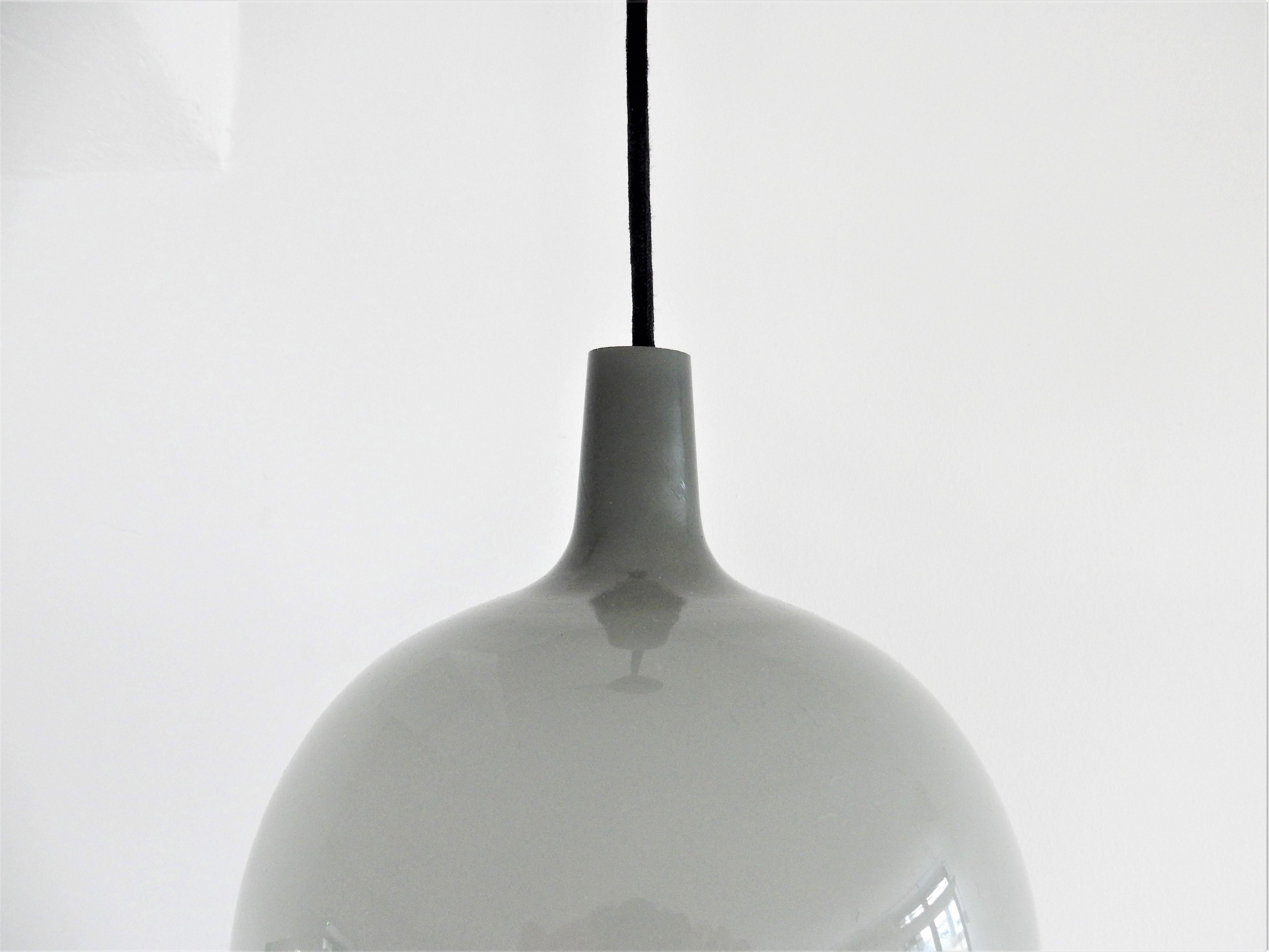 The Pompei pendant lamp was designed by Jo Hammerborg in 1963 for Fog & Mørup. Holmegaard produced the glass for this lamp. This model was made in green, grey and orange glass with a white inside. This beautiful grey variant is in a very good