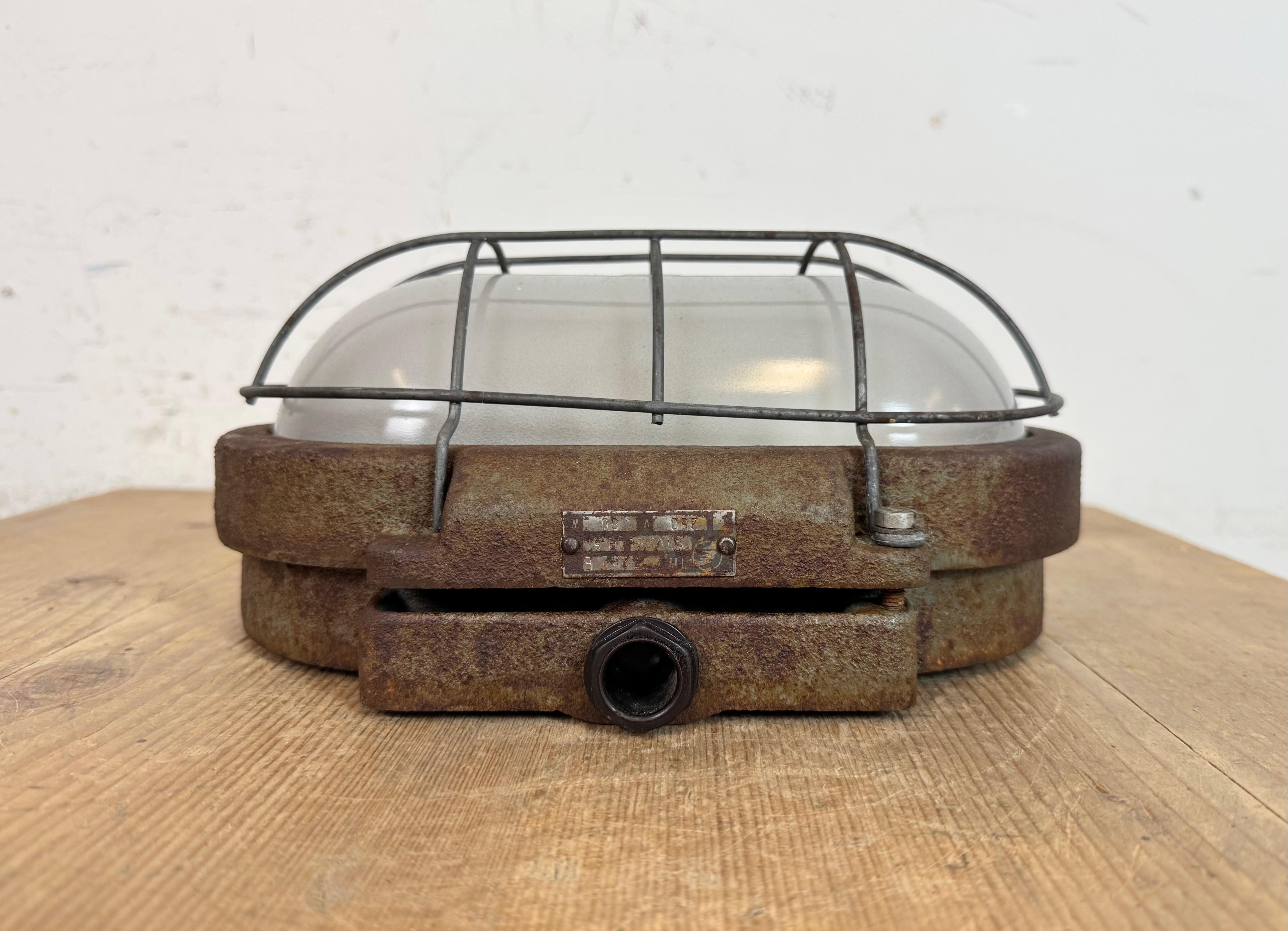 Industrial wall light made by Elektrosvit in former Czechoslovakia during the 1960s. It features a cast iron body, a milk glass cover and a steel grid.The porcelain socket requires E27 / E26 light bulbs. New wire. The weight of the light is 4 kg.