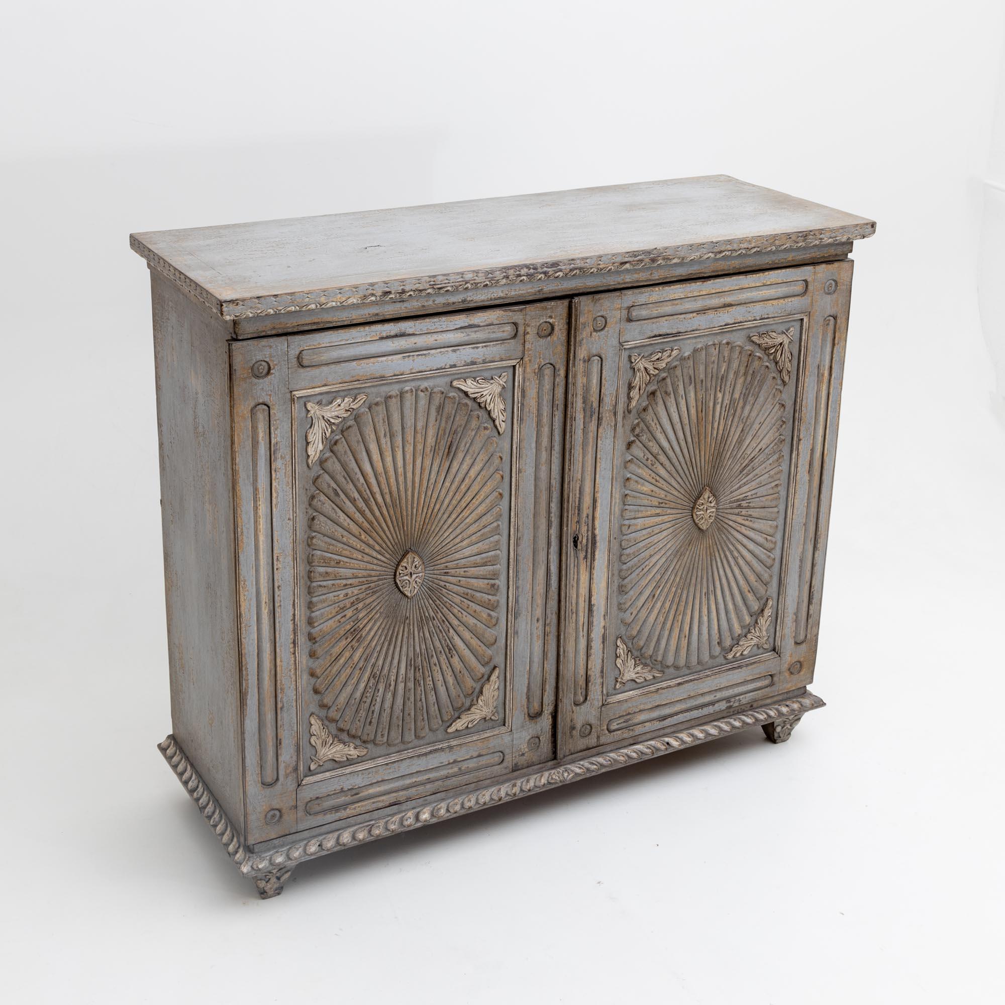 Two-door Indian sideboard with carved decorations on the doors and as surrounding friezes on the base and top plate. The grey frame is new and has been decoratively patinated.