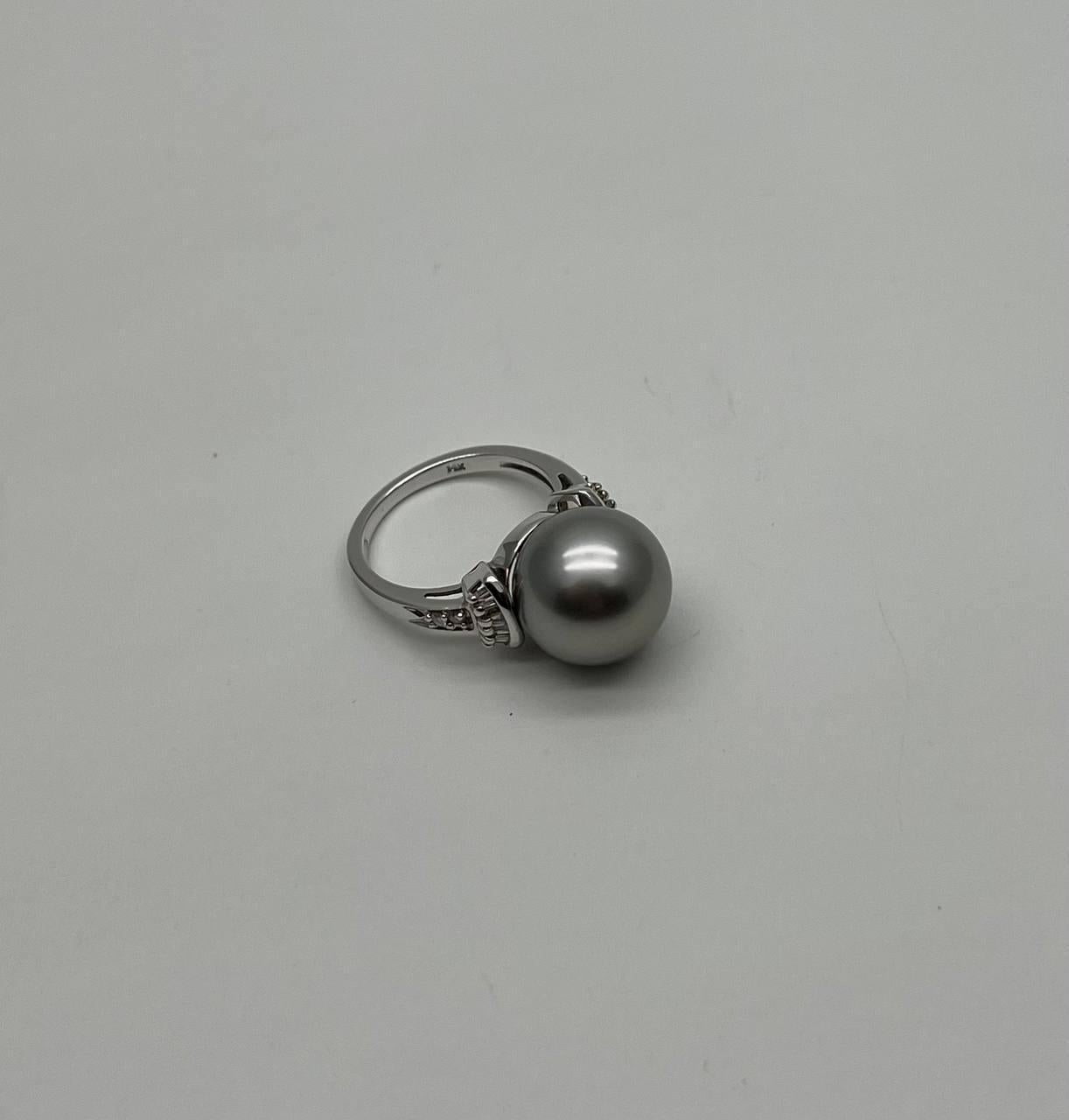Dieser elegante Ring besteht aus einer großen, schimmernden grauen Perle, die in ein schlankes Band eingefasst ist. Die Perle wird von kleinen, funkelnden Diamanten flankiert, die dem Design einen Hauch von Brillanz verleihen. 14K Weißgold. 0,79 CTW