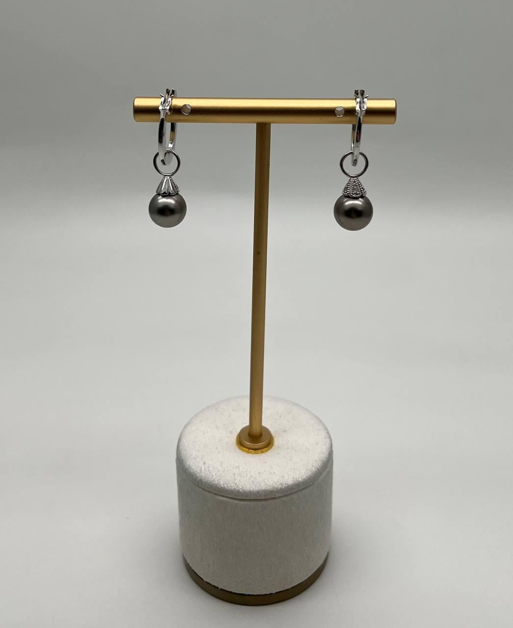 Descubre la elegancia de estos exquisitos pendientes.
Con lustrosas perlas negras de Tahití, estos pendientes son un testimonio de refinada artesanía.
Las perlas están suspendidas de aros delicados y texturizados, y los abrazos de diamantes añaden