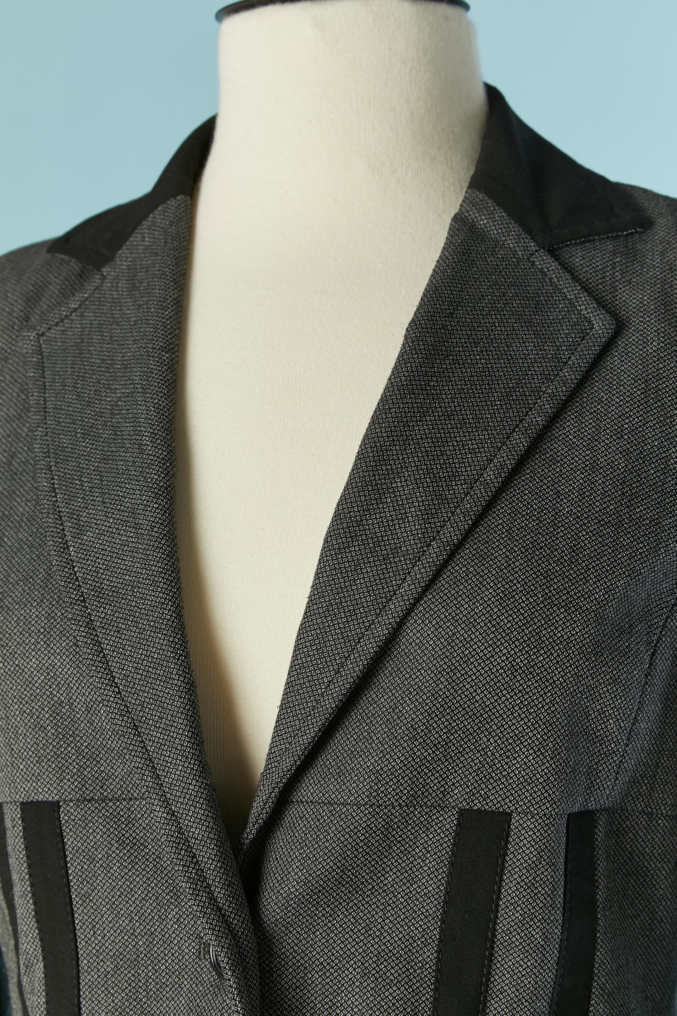 Grauer Rockanzug mit schwarzer Rillenapplikation. Zusammensetzung des Stoffes: 67% Polyester, 29% Viskose, 4% Elasthan. 
Dünnes Schulterpolster. Markenknopf und Knopfloch in der vorderen Mitte und an den Manschetten. Tasche auf beiden Seiten.
SIZE