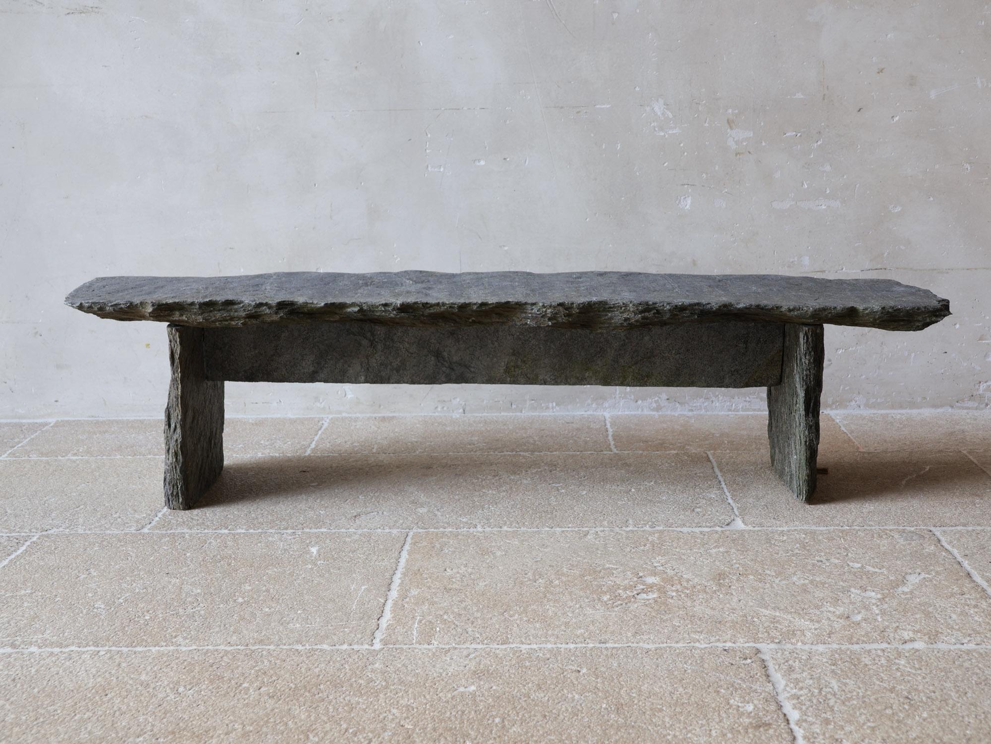 A grey slate (stone) coffee table, inspired by wabi-sabi and mountain cabin styles. It also fits perfectly in Axel Vervoordt style interiors. Made from hand-hewn antique slate slabs, it showcases a unique, rustic charm. This low and narrow piece
