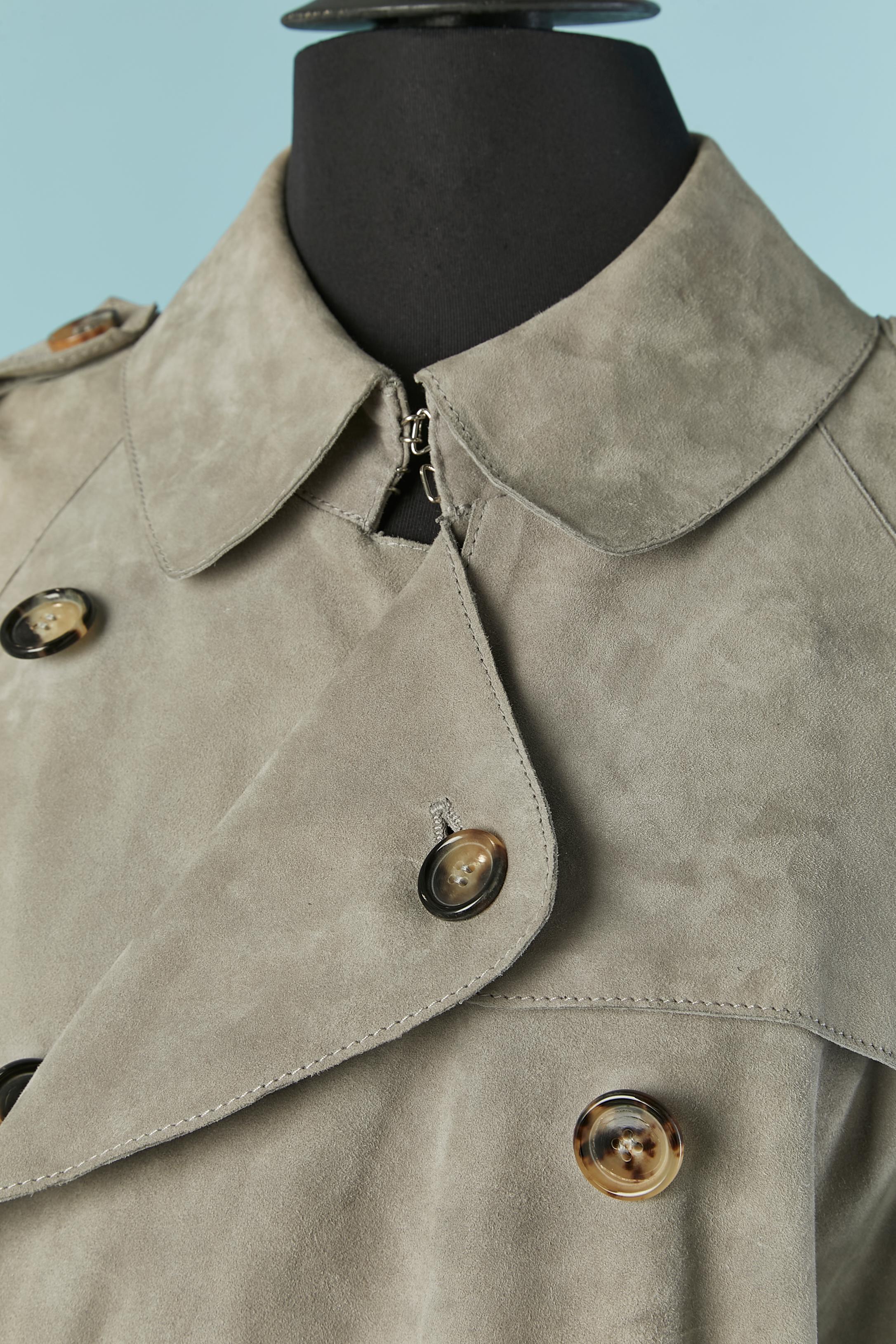 Trench in camoscio grigio con fodera in seta. Manica raglan. Cintura con chiusura a fibbia e passante. Piccola cintura e fibbia anche all'estremità della manica. Tasca su entrambi i lati con chiusura a bottone e asola. 
Spaccato sulla parte centrale