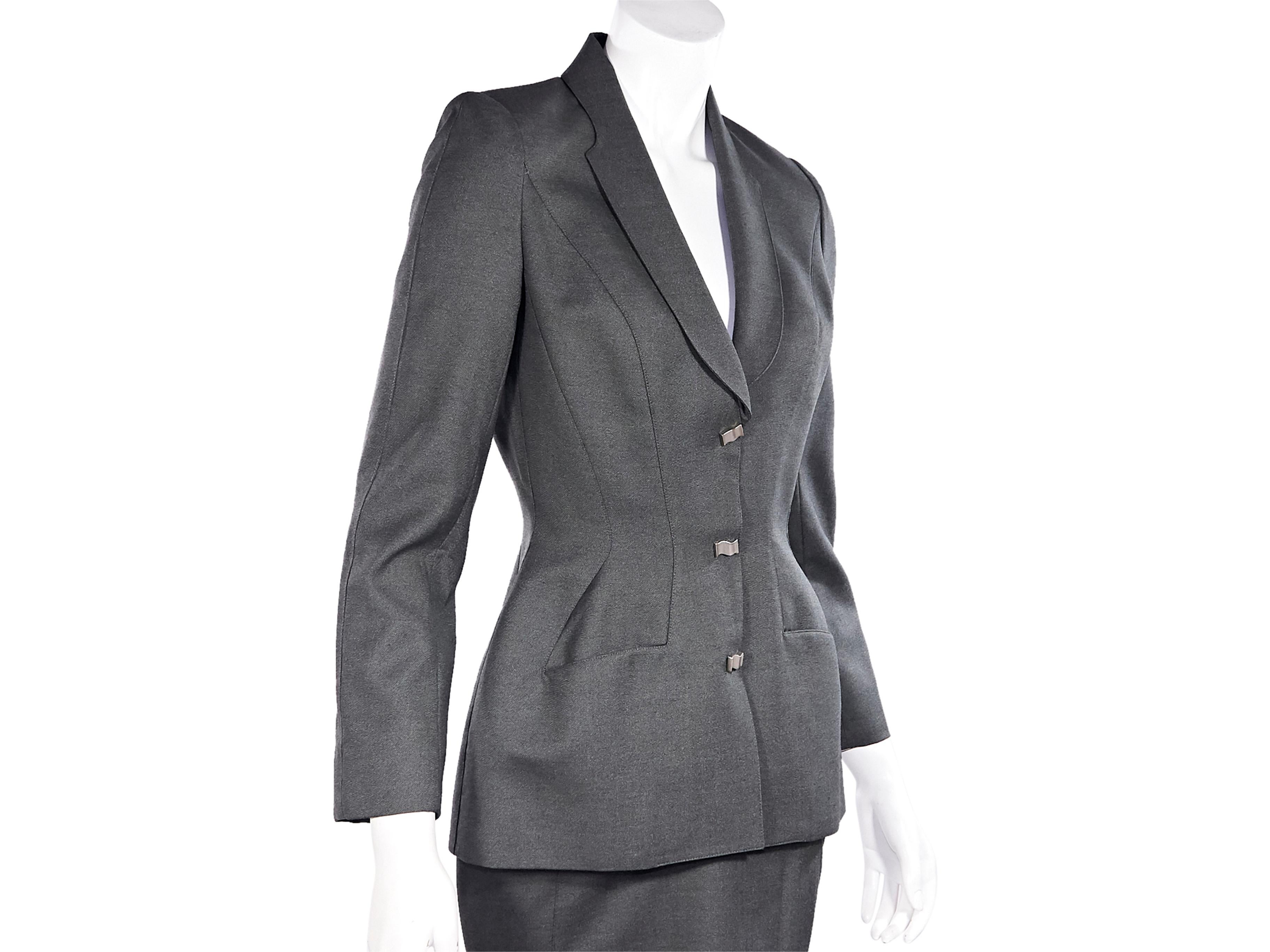 Product details:  Vintage grey wool skirt suit set by Thierry Mugler.  Rounded lapel.  Long sleeves.  Button-front closure.  Seam details create a fitted silhouette.  Silvertone hardware.  Matching pencil skirt.  Banded waist with back button and