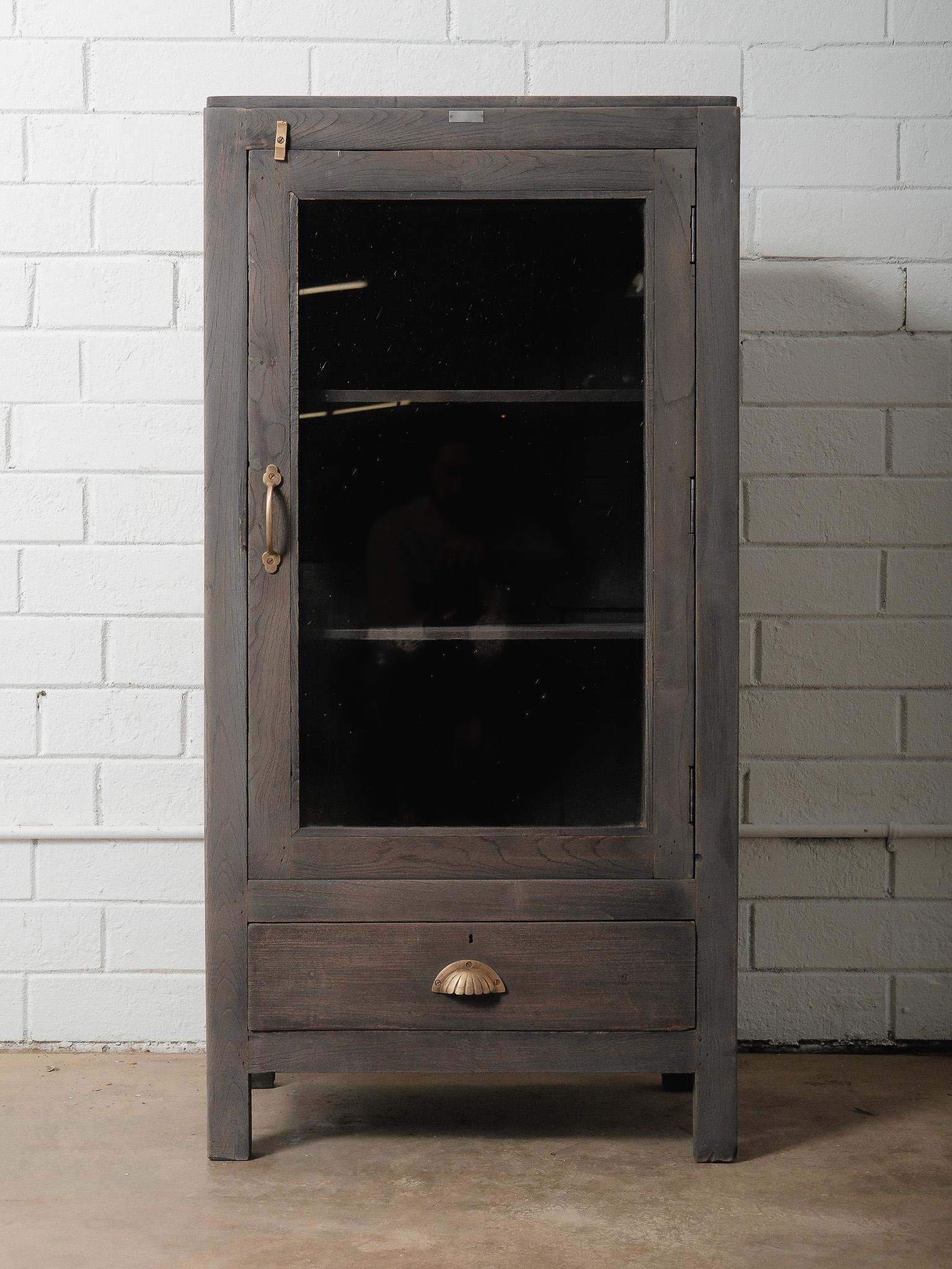 Cette armoire vitrée en bois, riche en caractère, est dotée d'une finition gris délavé qui met en valeur le grain et la texture naturels du bois. Probablement fabriquée au XXe siècle, l'armoire présente une seule porte vitrée et des étagères
