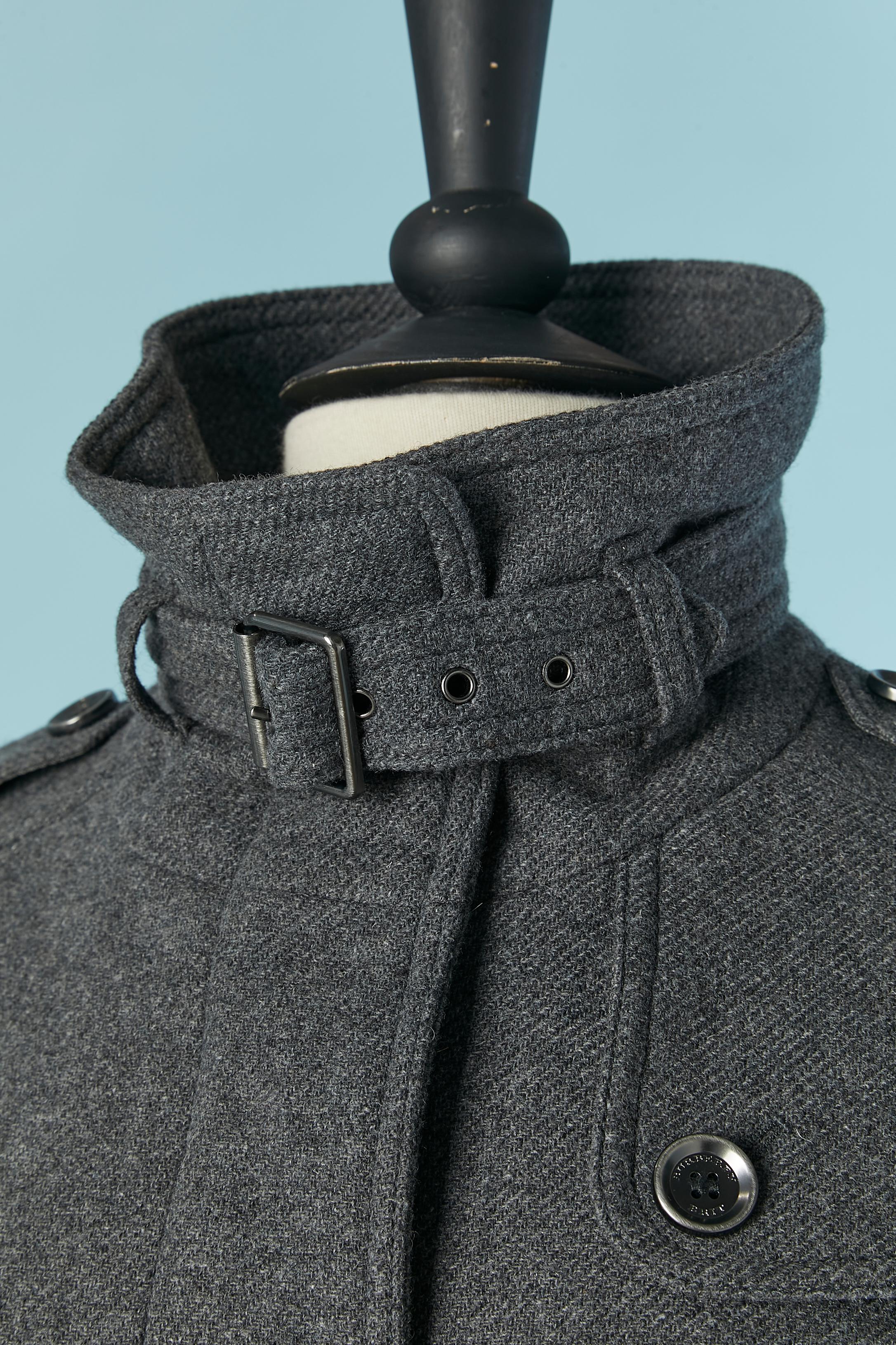Grey wool single breasted coat. Main Fabric composition: 65% wool, 3% nylon, 5% cashmere. Rayon lining. Hidden branded button and buttonhole closure on the middle front. Belt in fabric and metal buckle and belt-loop.  Strap on the end of the sleeve