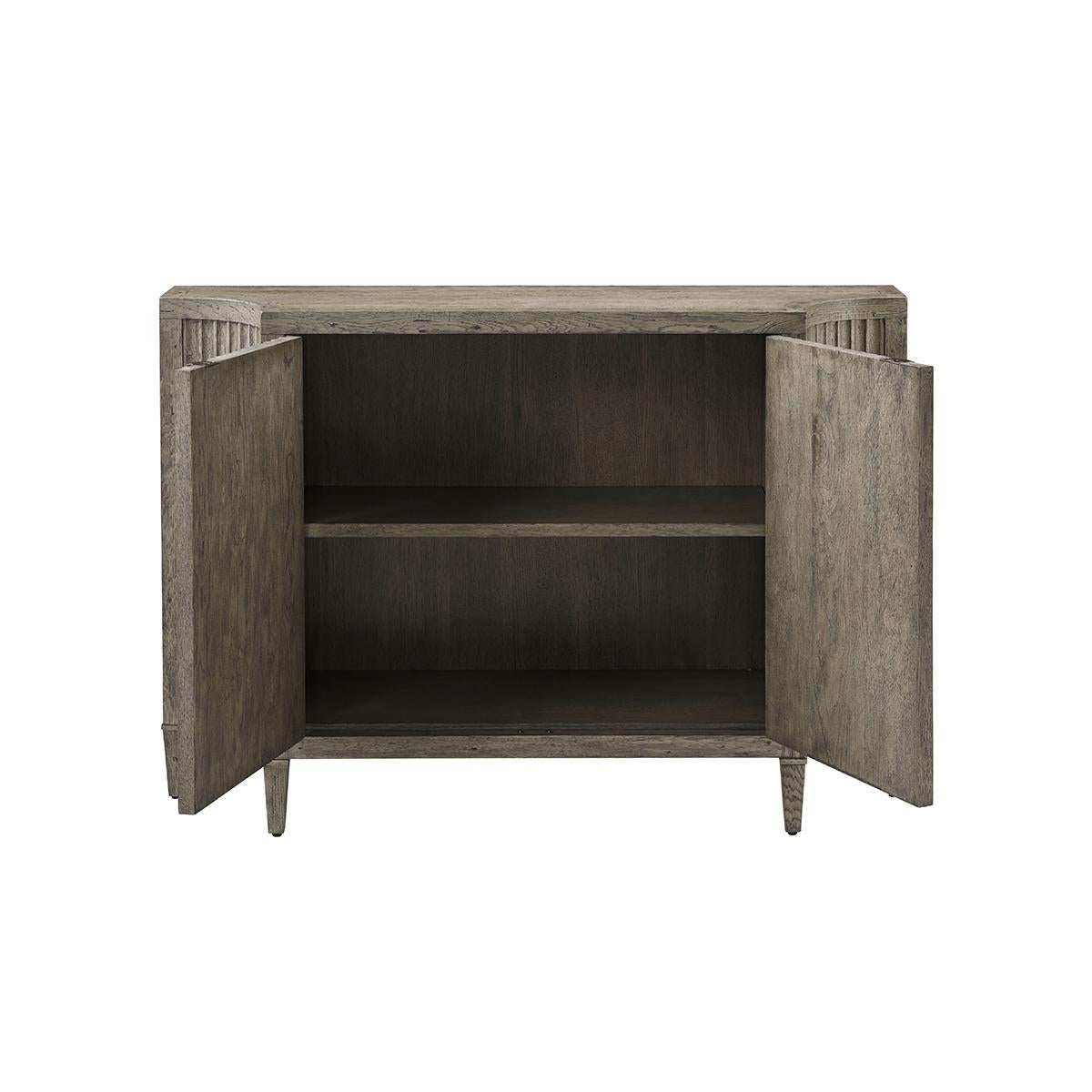 A modern rustic oak credenza taking form from French antiques of the 18th century. With walnut fluted doors, flanked by incurved ends, with a shaped top with parquetry inlaid decorations. The two-door cabinet opens to an interior, ideal for storage,