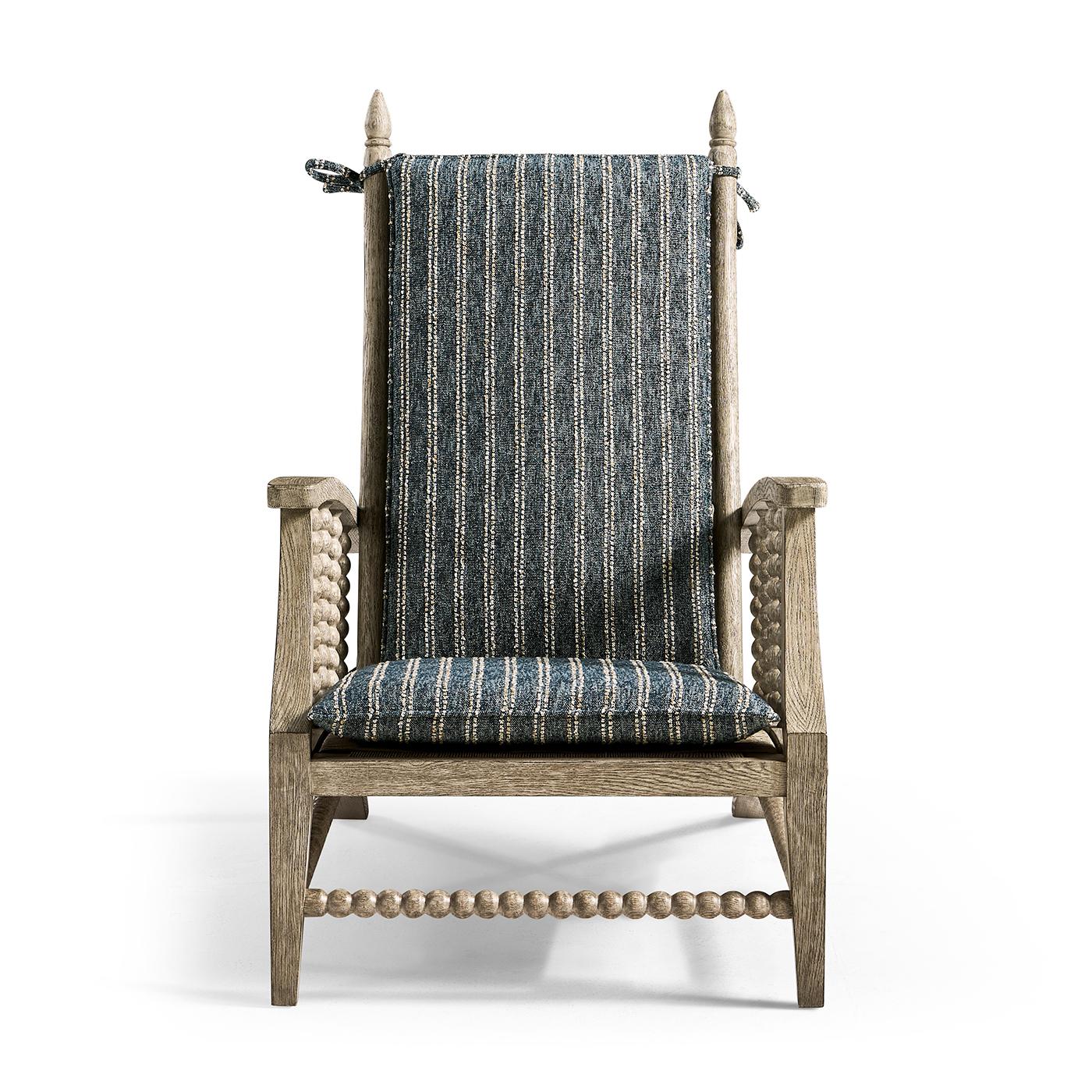 Con una forma elegantemente inclinada, proporciona una experiencia de asiento relajada pero refinada para salones, dormitorios o invernaderos. Su armazón de roble macizo en acabado grisáceo presenta tallas intrincadas, mientras que el tejido y el