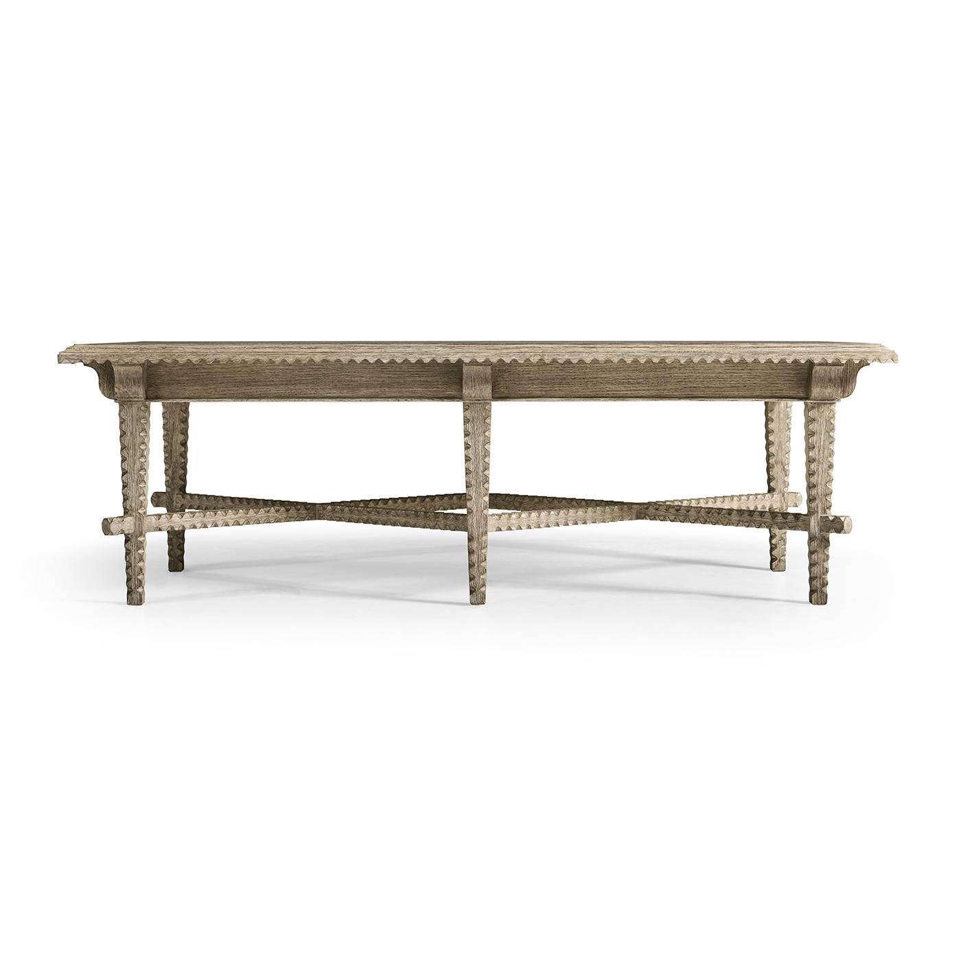 Featuring tramp-style carvings that add a touch of artisanal detail, this table showcases a greyed oak finish for a relaxed, airy feel. Its finely detailed legs and subtle cross-stretcher design enhance its rustic appeal, making it an exquisite
