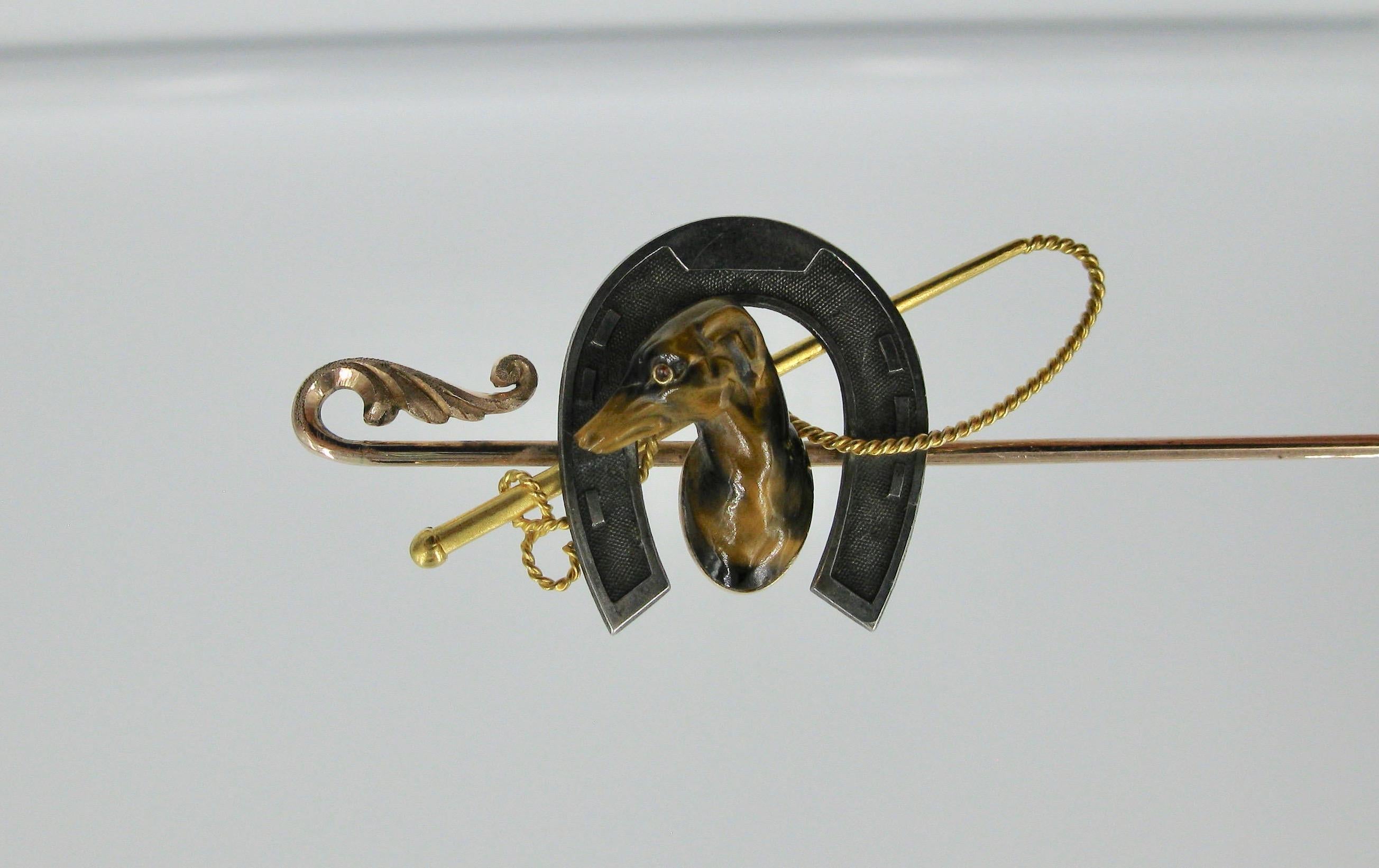 A very special and rare Sporting Horse Greyhound Racing Hat Pin Brooch depicting a Greyhound Dog beautifully carved in Tiger's Eye.  The greyhound is set within a silver horseshoe with a 14 Karat gold riding crop on a gold hat pin.  The carving of