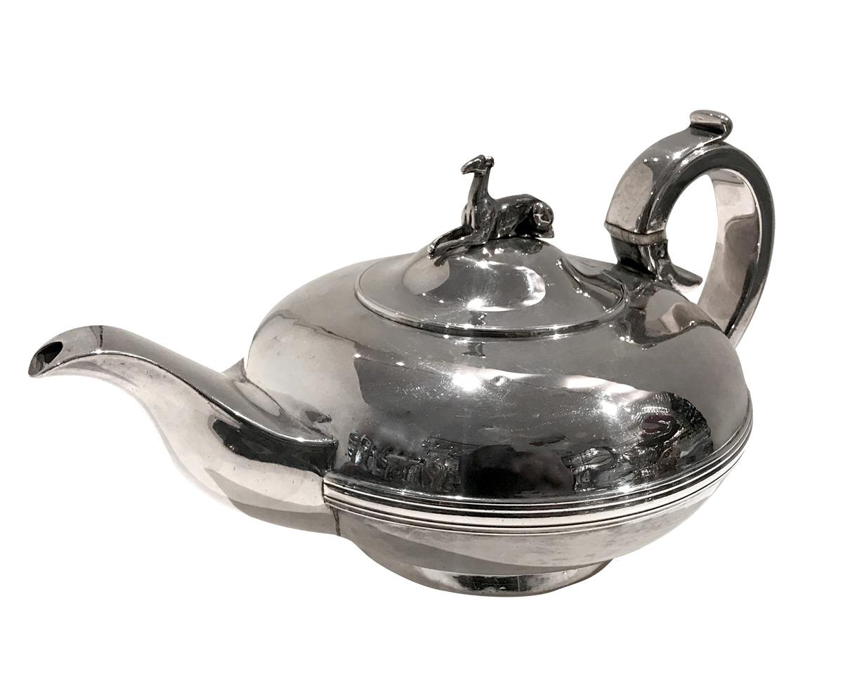 This sterling silver English teapot in circular shape with just a classy reeded band across the body, and shaped spout. The teapot is enhanced on its hinged lid with a lying dog knop, a greyhound. Stylized scrolled handle and circular base.
So