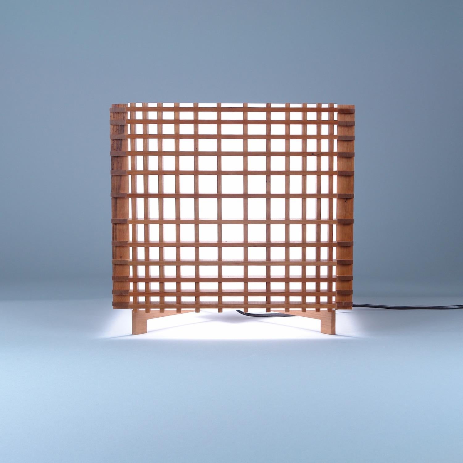 Grid Cube table lamp in Scandinavian and Japanese influenced Contemporary style. Cherry and Acrylic.
The rectilinear forms of the diminishing grid give a paradoxical illusion of circularity, of foreground and background.
Electric components UL