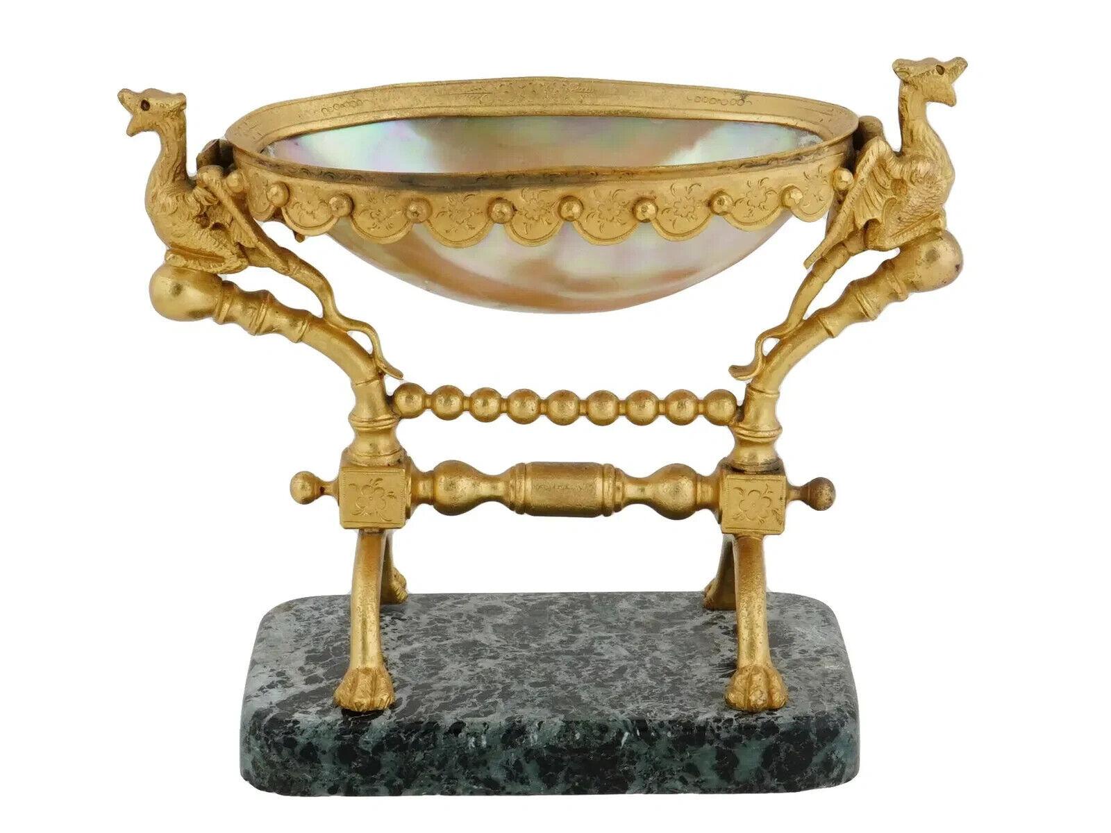 A vintage French manner patinated bronze ware featuring a mother of a pearl dish. The design showcases two intricately crafted griffin figurines that serve as supports, enhancing the tabletop presentation. The oval bowl elegantly features scalloped