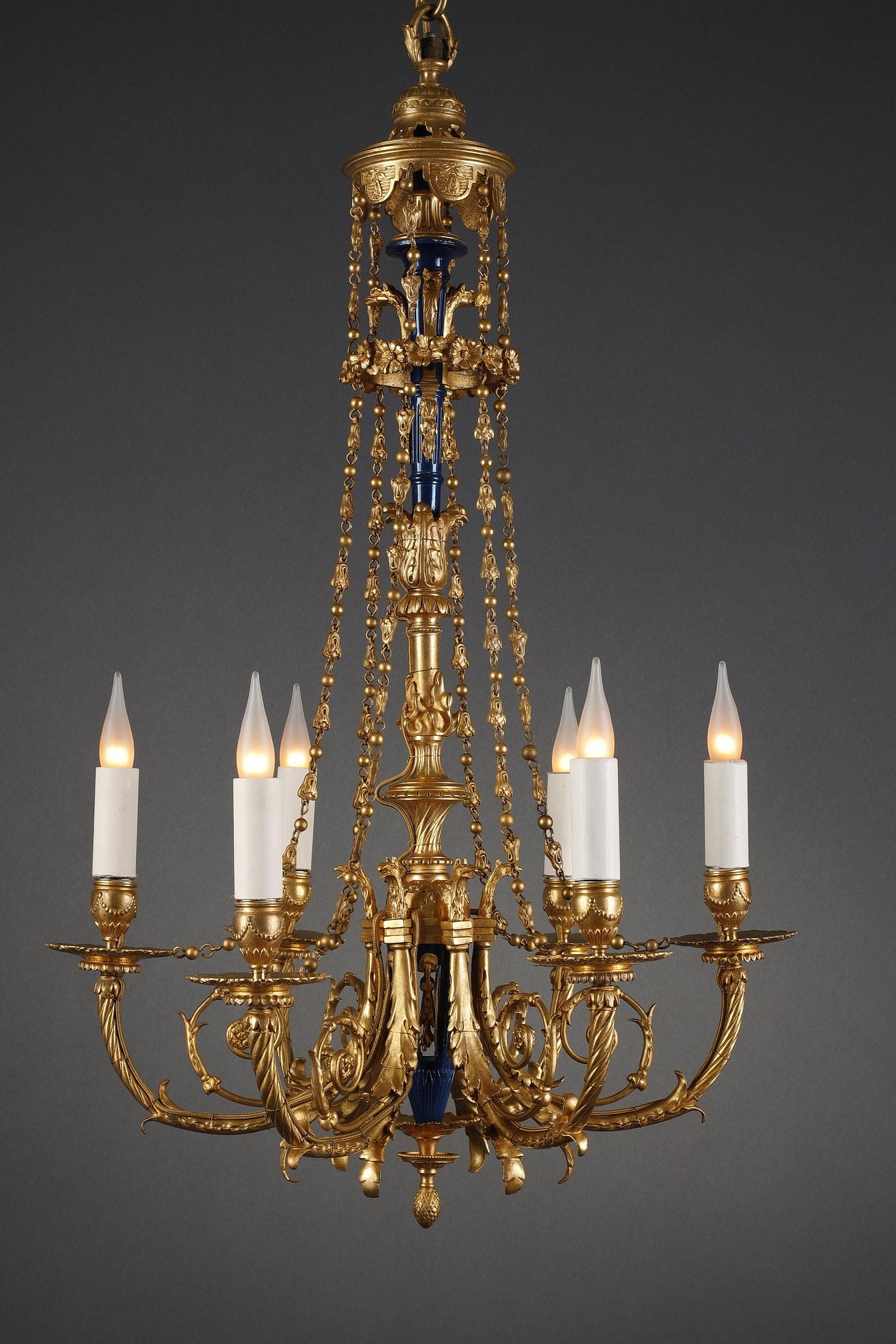 Charming Louis XVI-style chandelier in gilded bronze with six lights. The baluster-shaped central shaft, in gilded bronze and blue enamel is richly adorned with griffins heads, foliage and flames. It is lit by six light arms surmounted by griffins