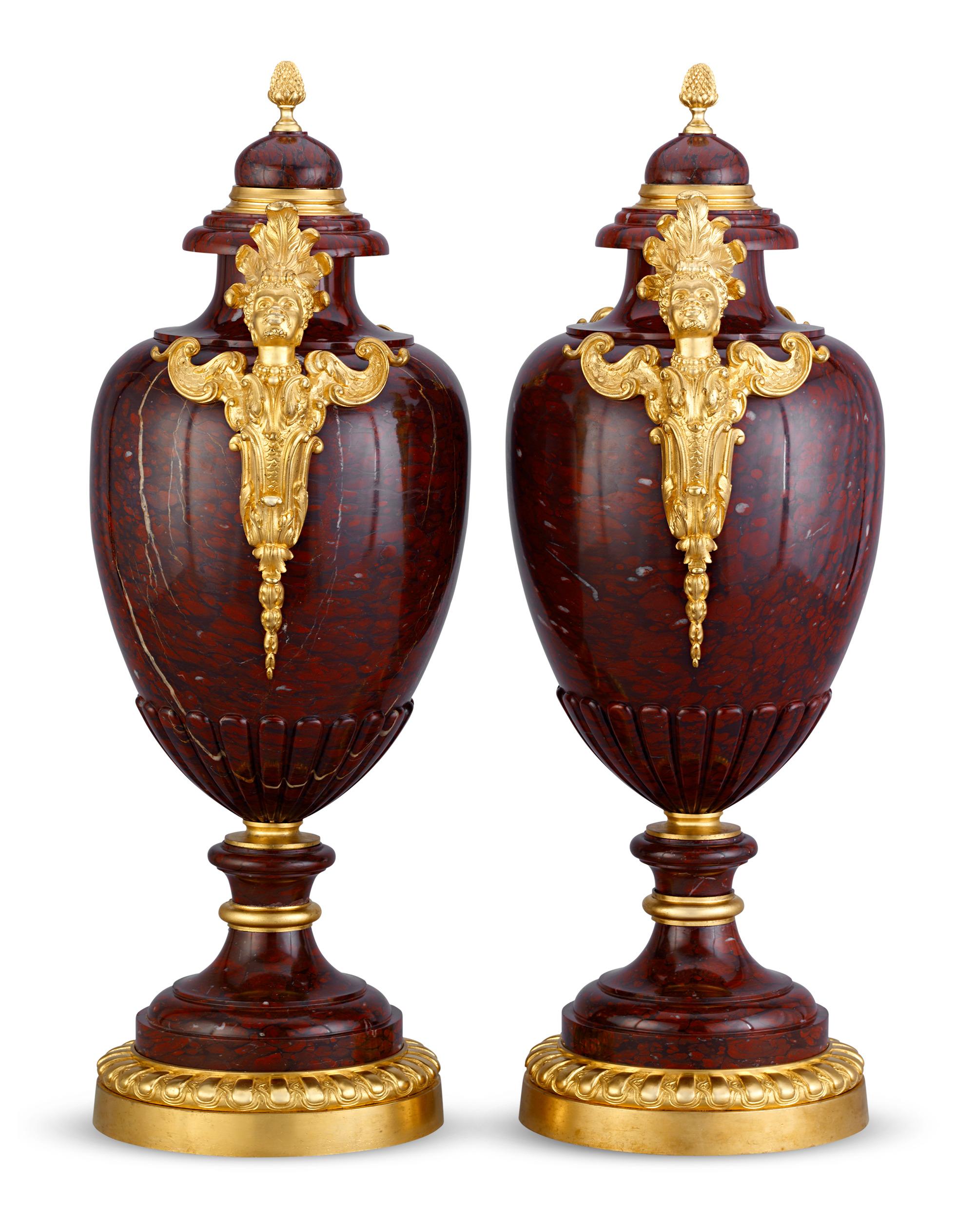 Fashioned of rare and precious griotte rouge marble and gilt bronze, these vases embody neoclassical elegance at its finest. Borrowing its forms and motifs derived from classical Roman and Greek antiquity, the gilt bronze contrasts beautifully with