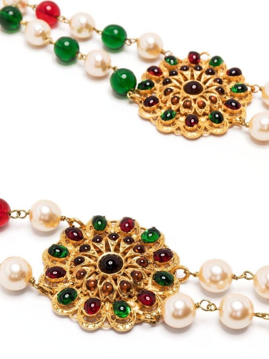 Designed by Gripoix in the style of Chanel, this vintage pre-owned necklace has been designed with two rows of red and green glass beads and faux pearls. Finished with two large gold-toned with flower motifs with red and green beaded detailing, this